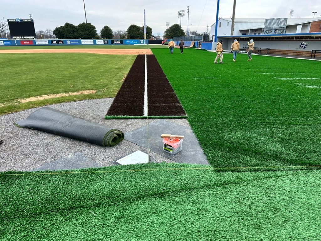 Baseball field with artificial turf installation in progress; green field and brown infield.