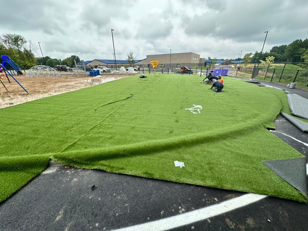 Workers installing green artificial turf on a playground with a black track. Construction site.