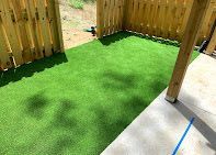 A small, fenced-in outdoor area with bright green artificial turf and a concrete patio.