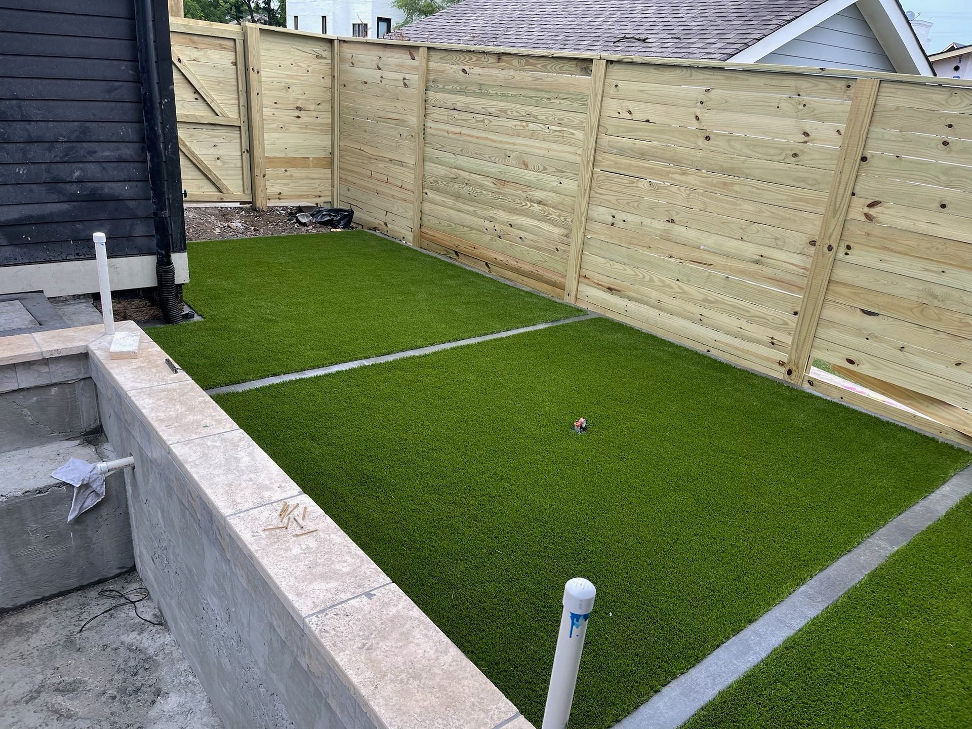 Small backyard with artificial turf, bordered by a wooden fence and concrete structures.