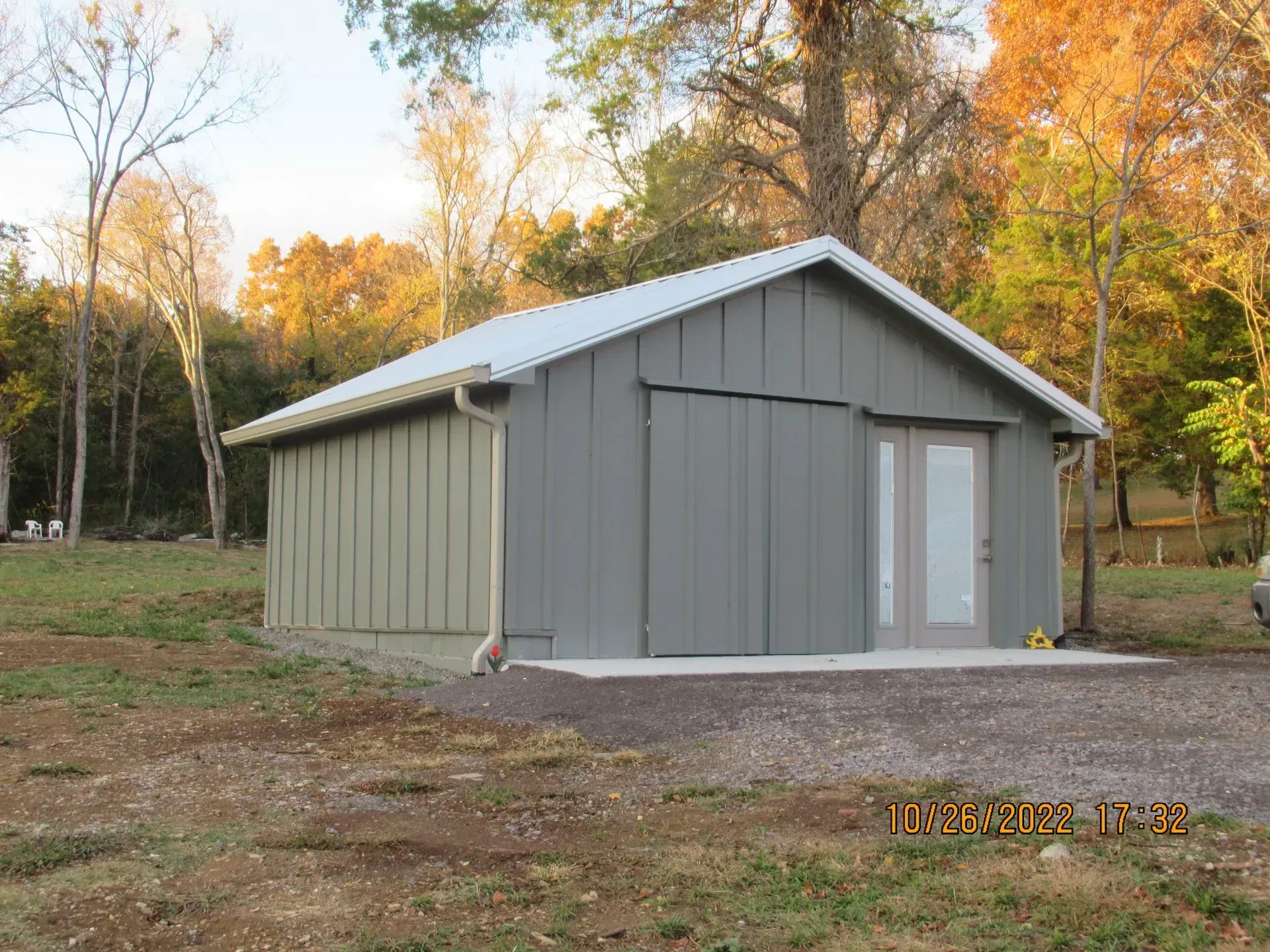 Gray metal shed in a wooded yard, with a white roof and double doors.