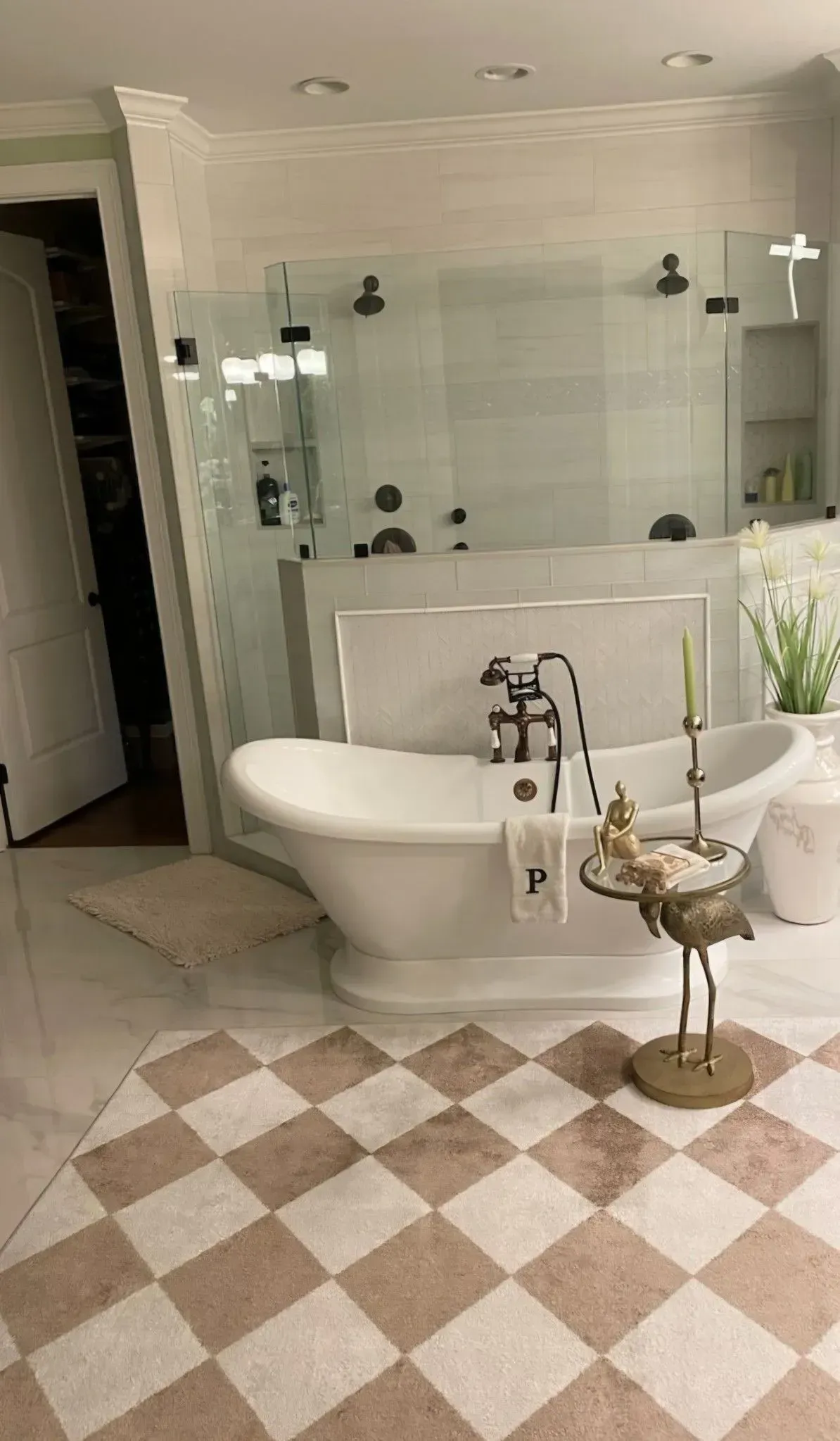 Elegant bathroom with a freestanding tub, glass shower, and pink-and-white checkerboard rug.