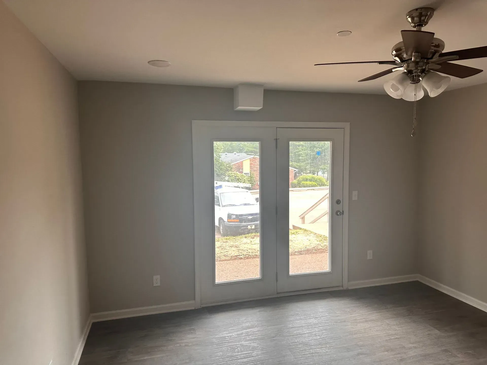 Empty gray room with double glass doors, ceiling fan, and dark floor.