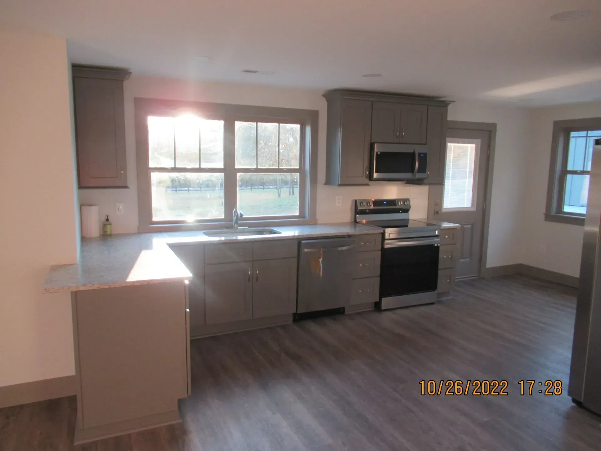 Bright modern kitchen with gray cabinets, stainless appliances, and a large window over the sink.