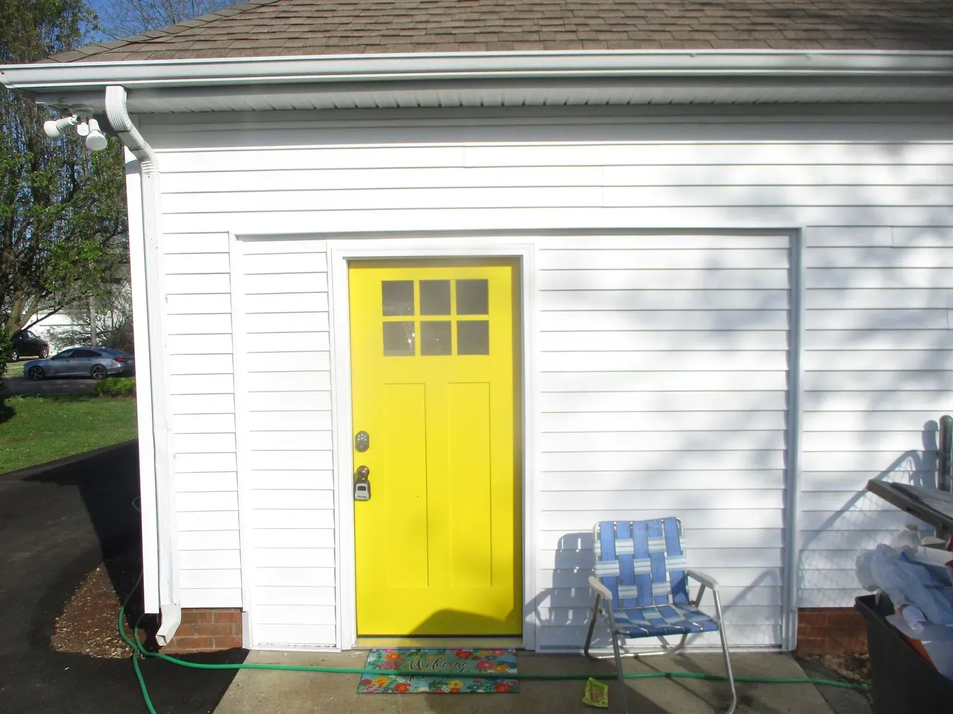 White garage with a bright yellow front door and two blue chairs on the porch