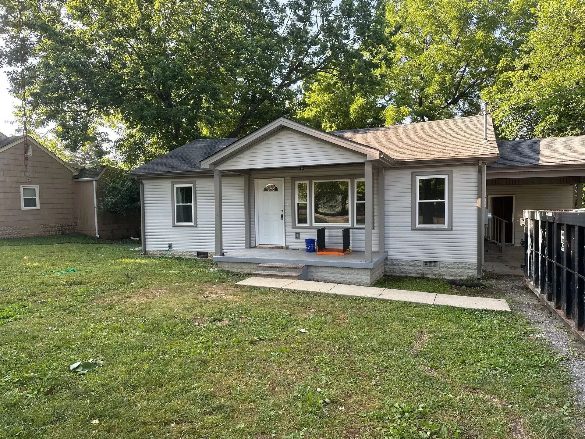 Small gray house with a front porch, white trim, and a grassy yard under trees