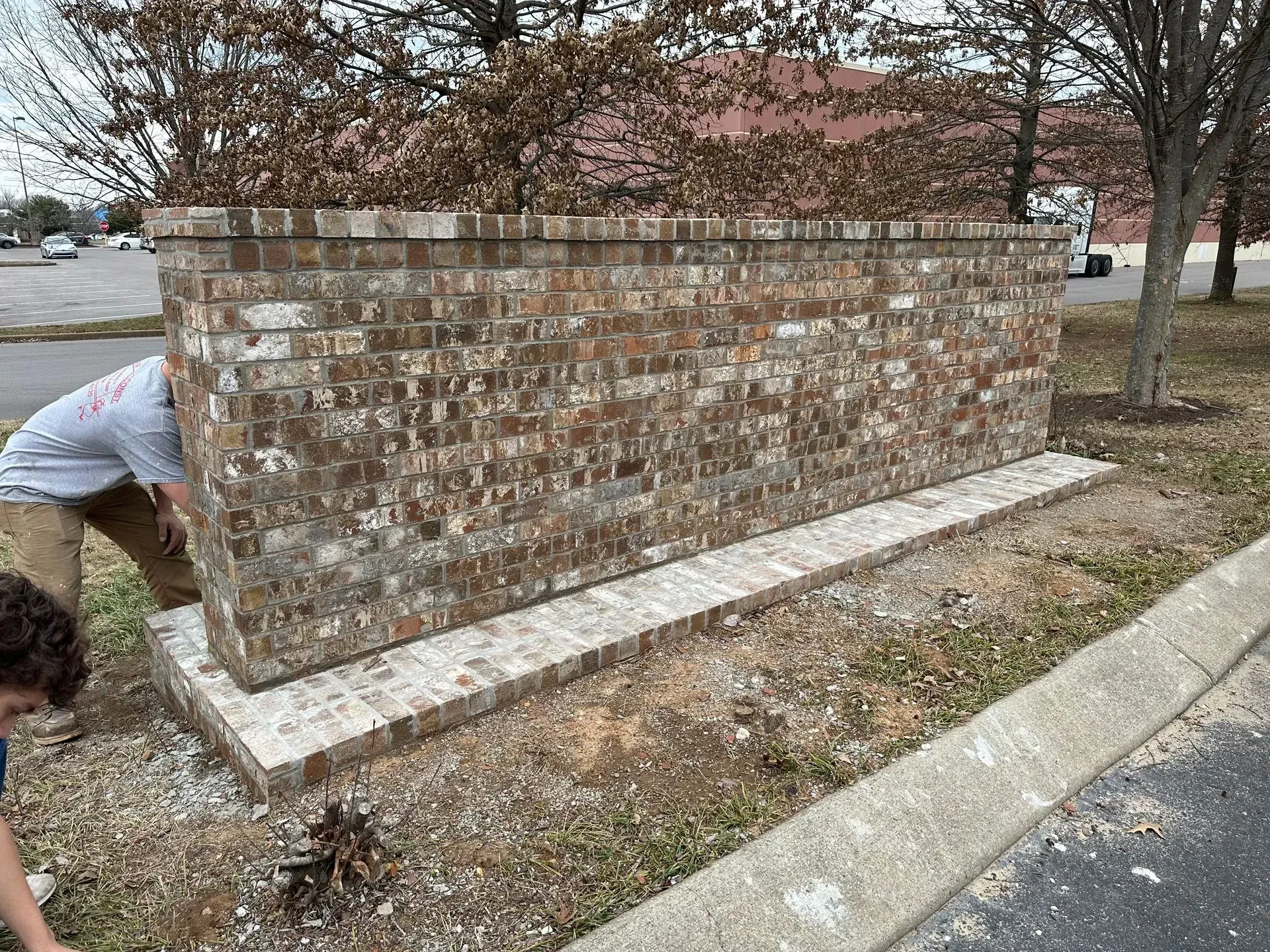 Brick retaining wall along a roadside, with two people working near its left end.