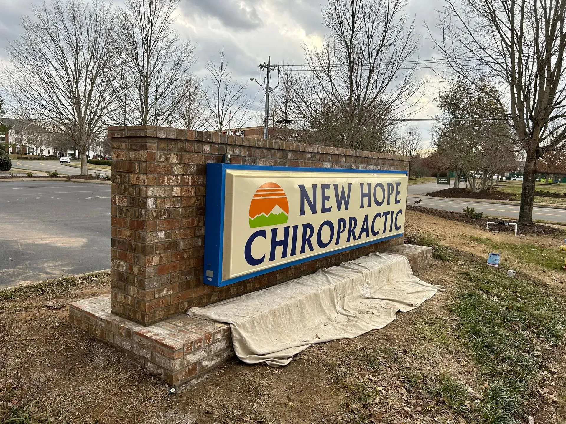 New Hope Chiropractic sign on a brick monument by a roadside, with trees and cloudy sky