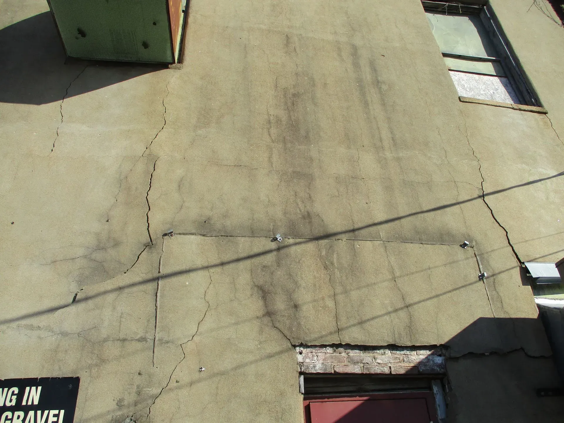 Cracked beige stucco wall with windows and a partial sign at the bottom left