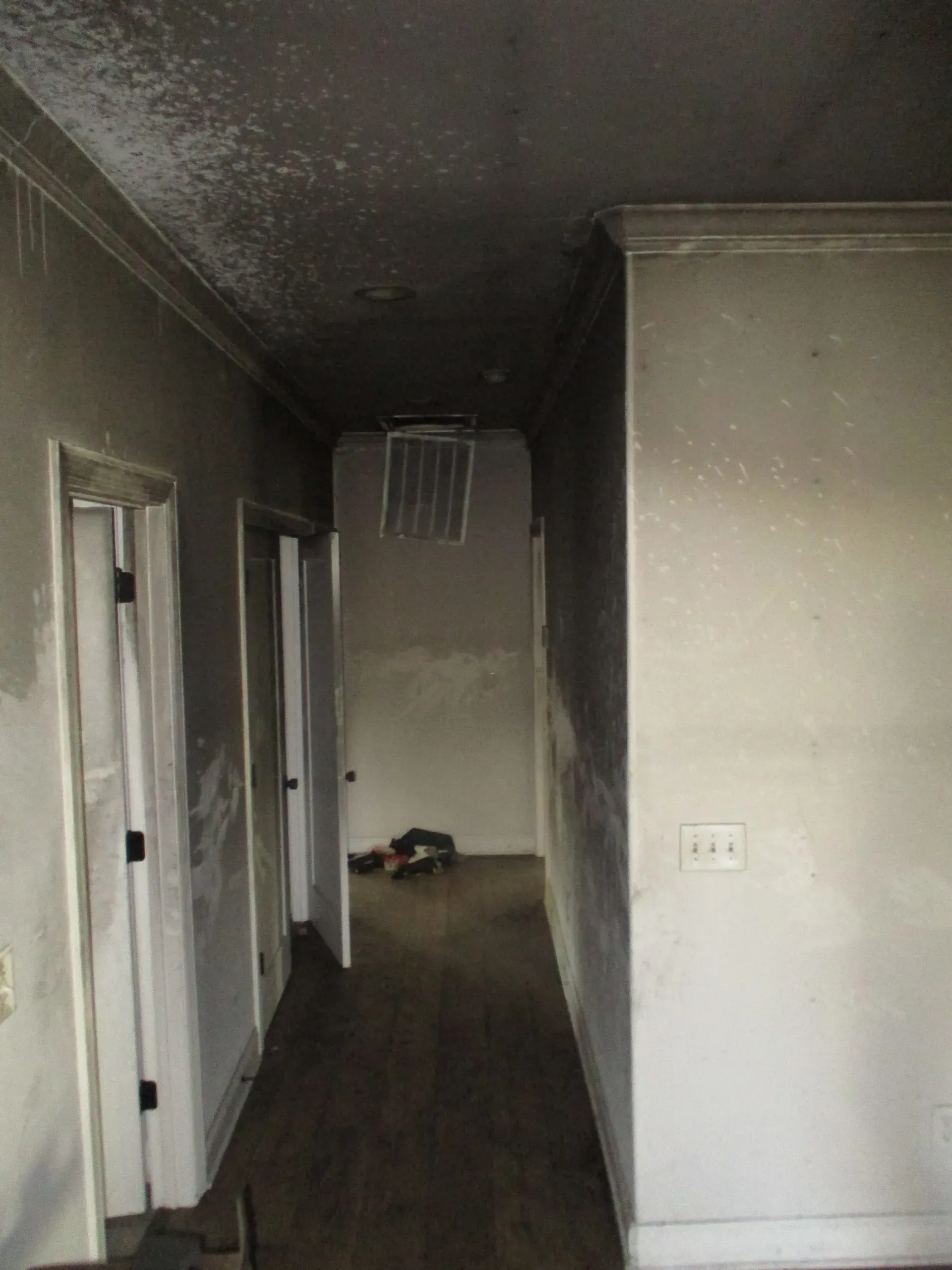 Dim hallway in an old house with dark floors, white walls, and a small pile of items at the far end.