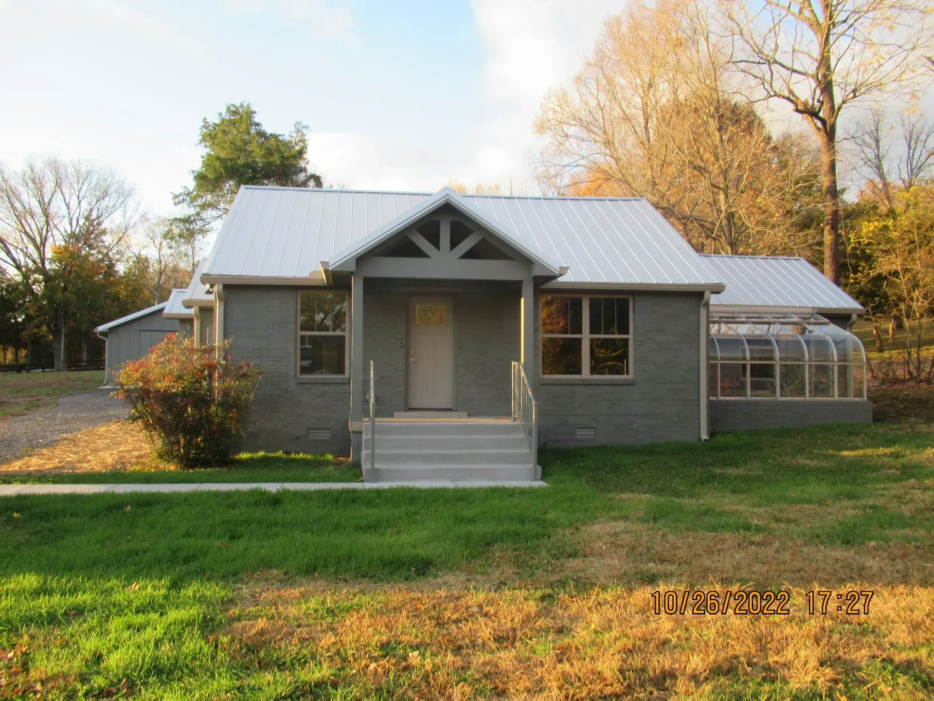 Small gray house with a metal roof, front porch, and grassy yard in warm evening light