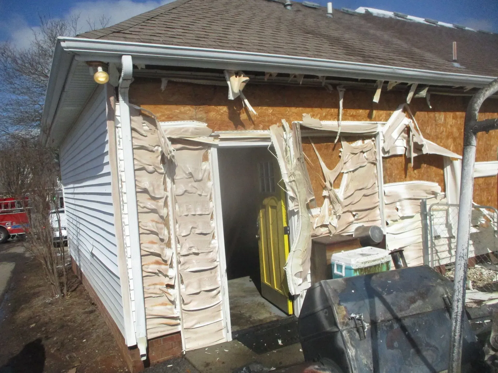 Partially demolished house with torn siding and debris around an open doorway
