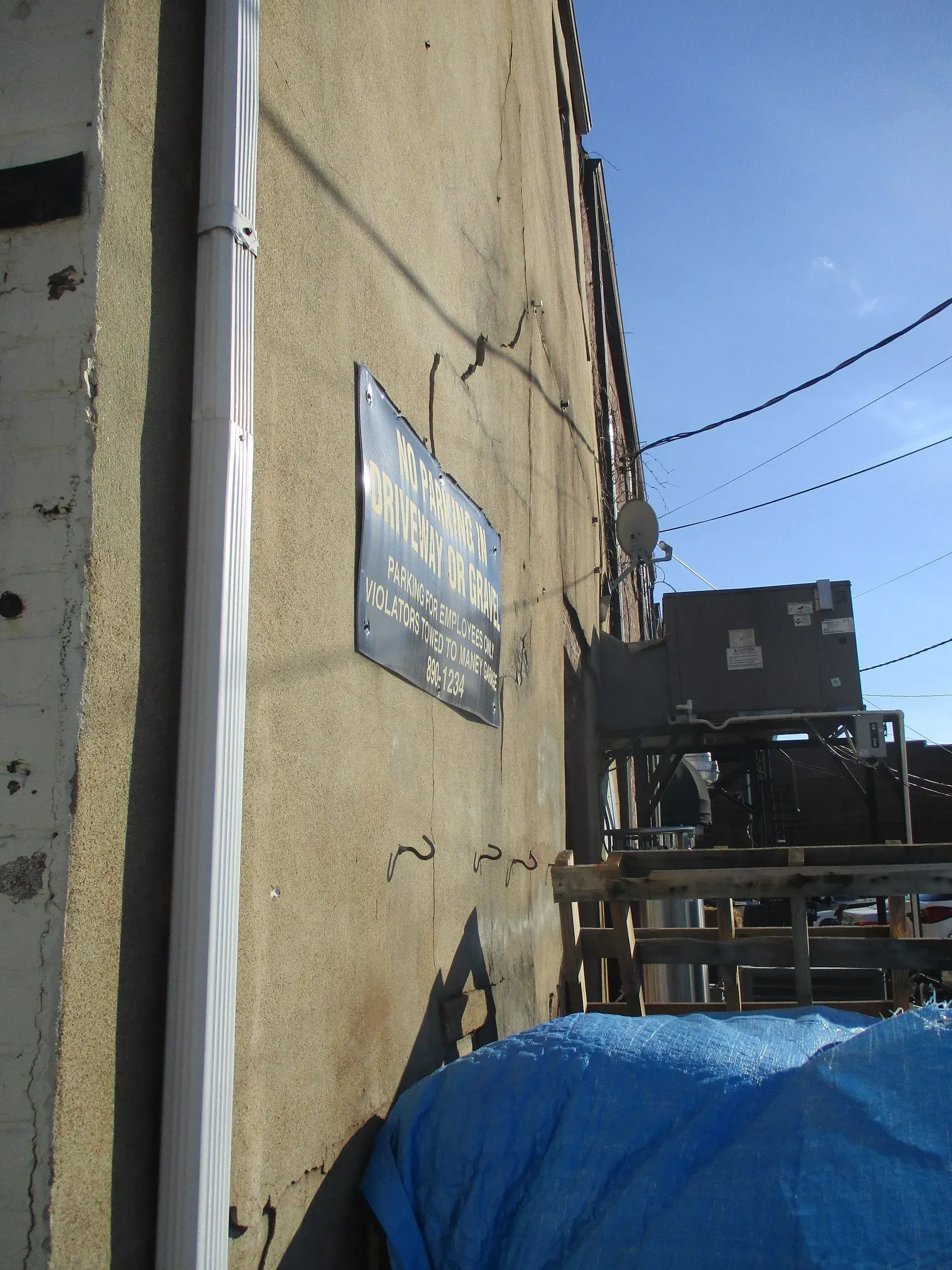 Sunlit alley beside a stucco wall with a sign, blue tarp, and overhead wires