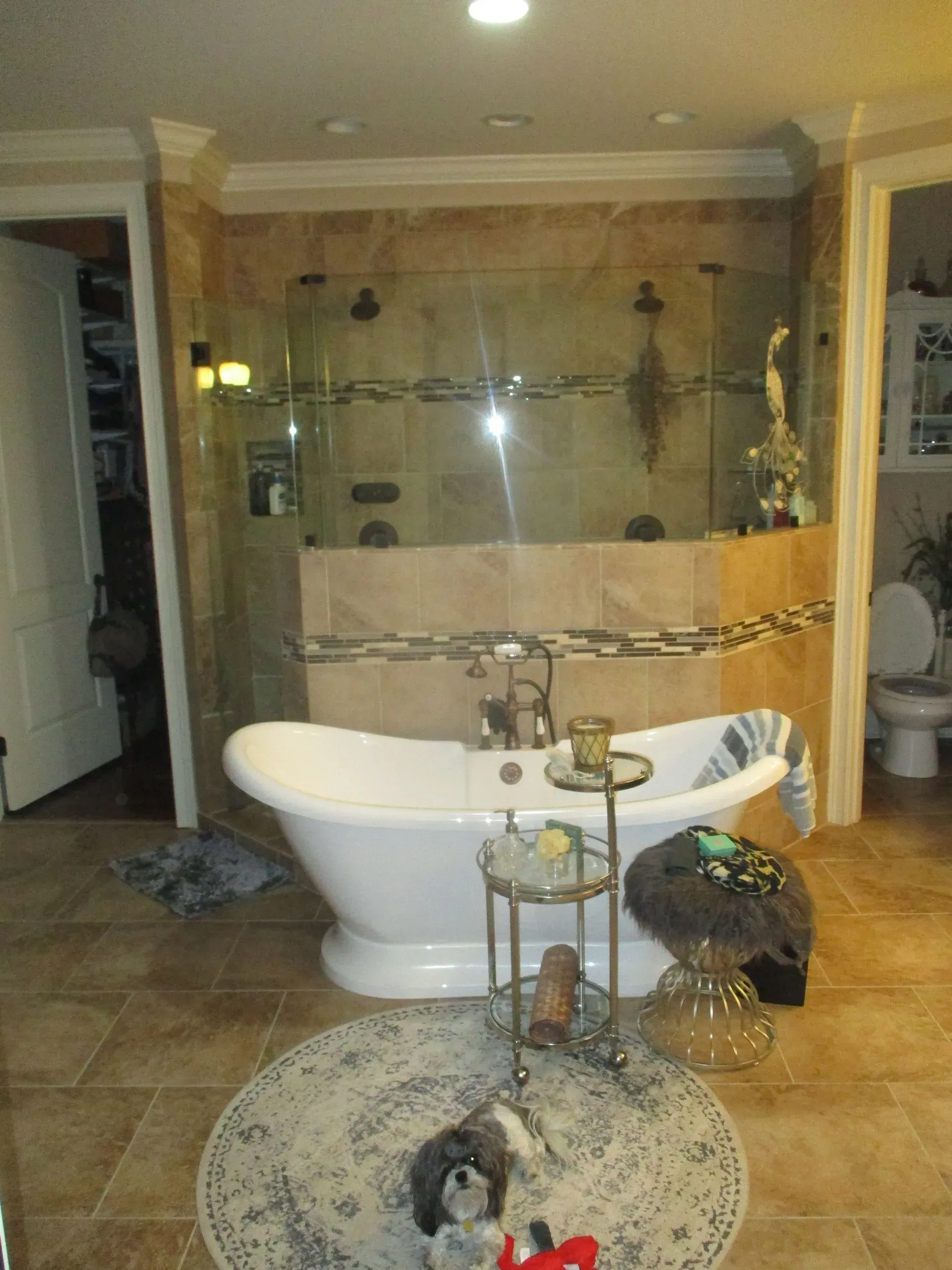 Bathroom with freestanding tub, glass shower, and decorative shelves; small dog on tiled floor.