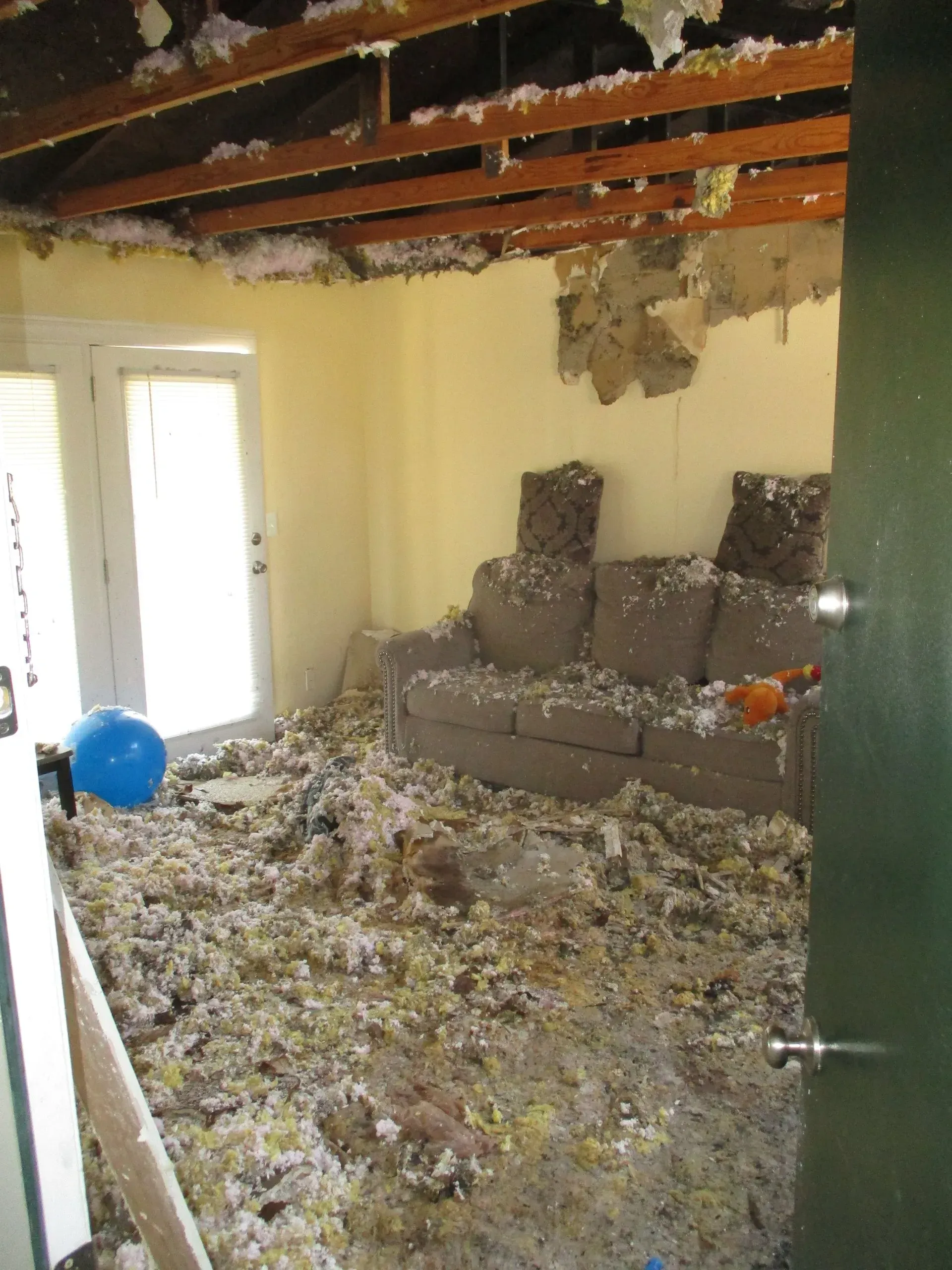 Damaged living room with collapsed ceiling, debris on floor, and a couch against the back wall