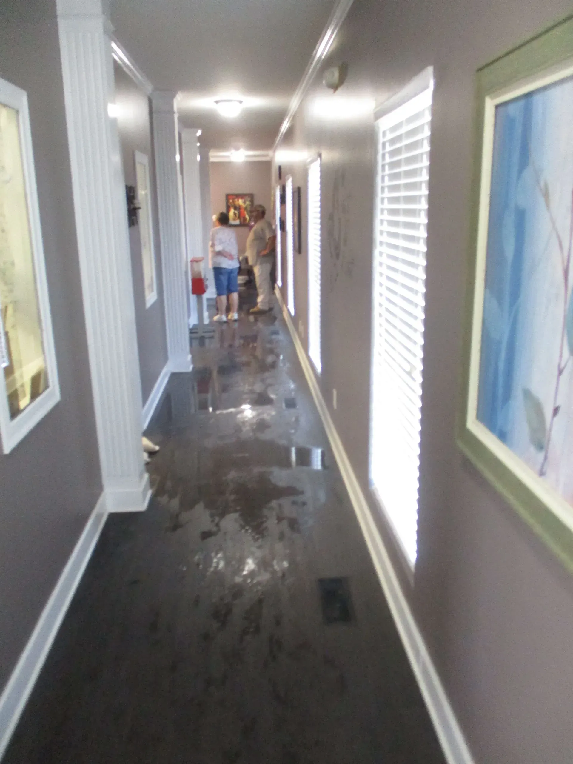 Narrow hallway with water on the floor and a person cleaning in the distance