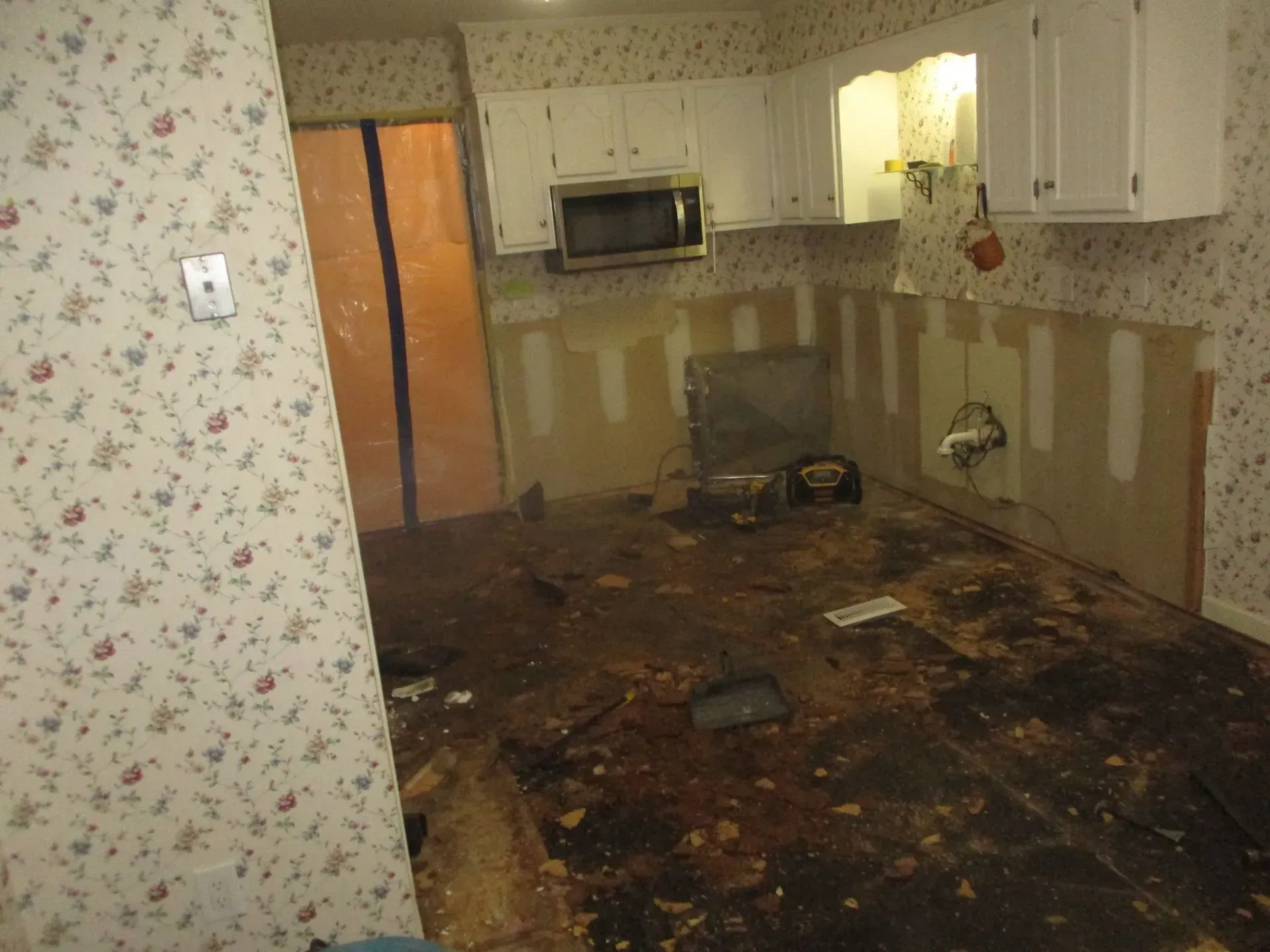 Burned kitchen with charred floor, damaged cabinets, and smoke-stained walls