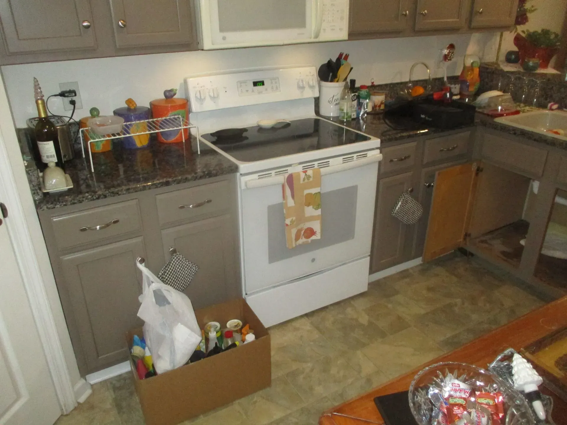 Cluttered kitchen with white stove, brown cabinets, and boxes on the floor.