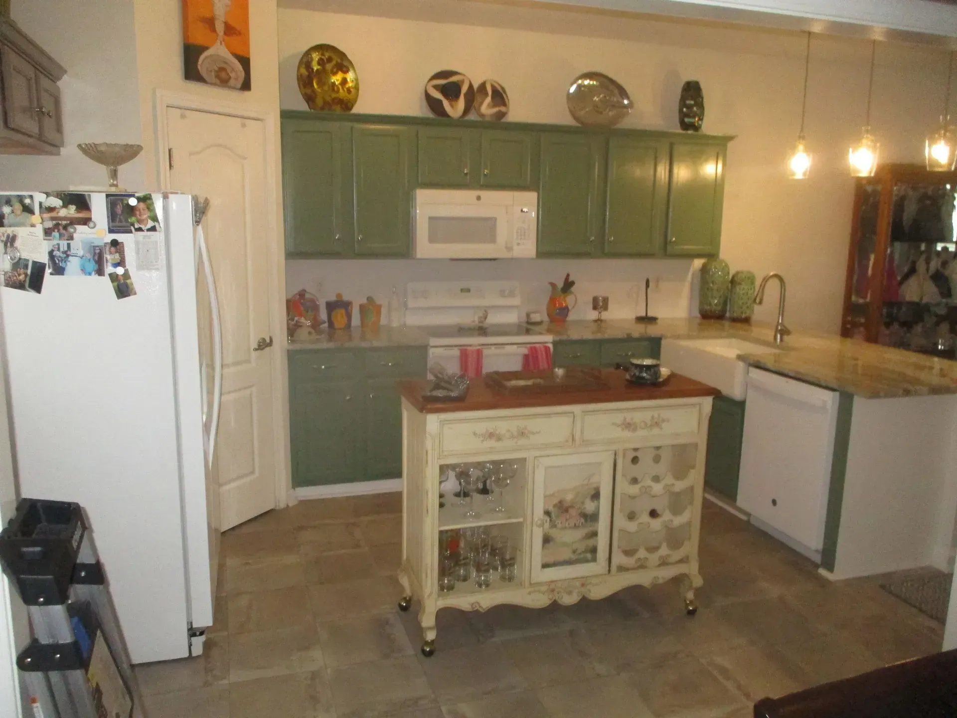 Vintage kitchen with green cabinets, white fridge, central island, and warm pendant lights