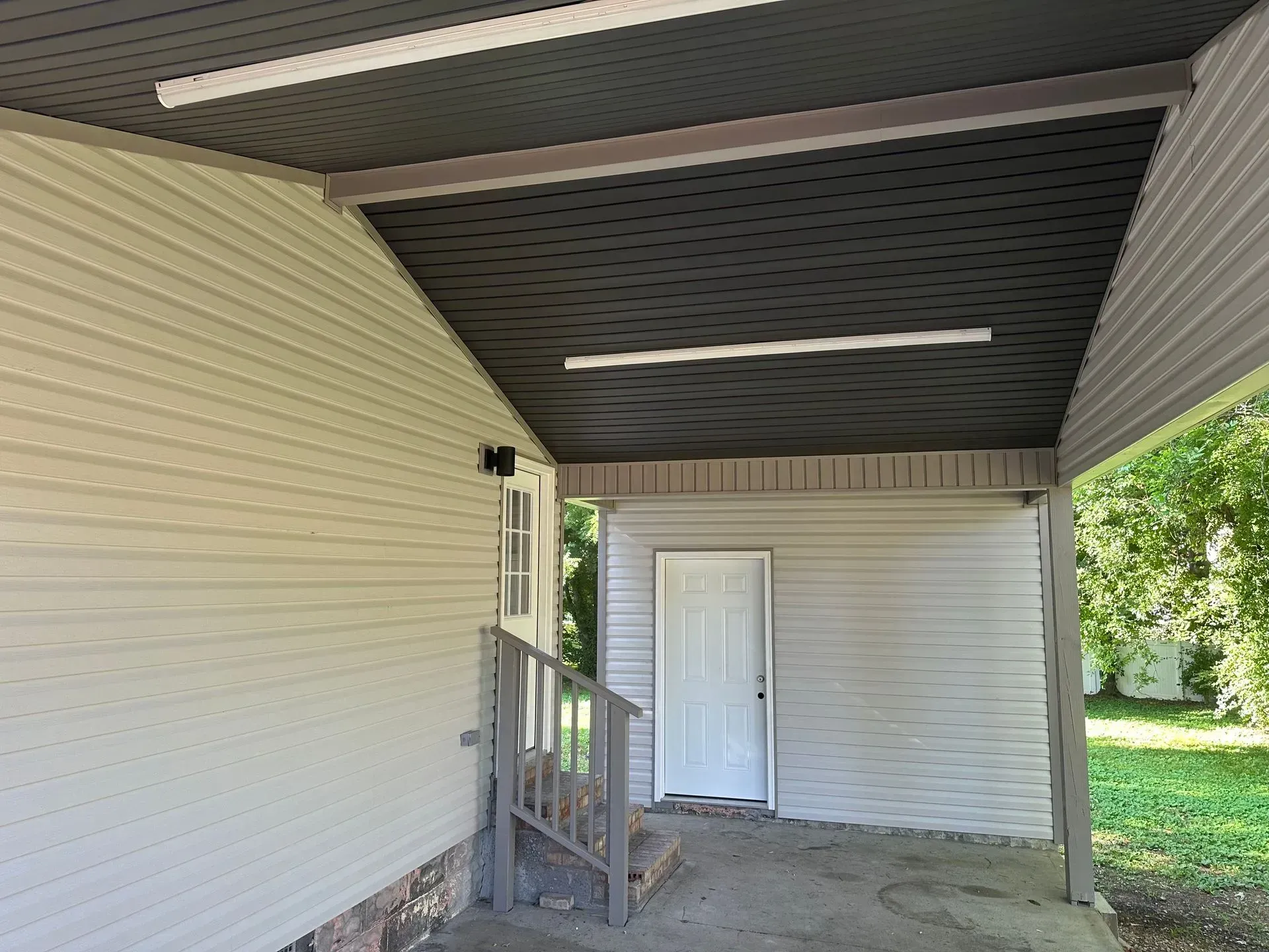 Covered porch with white siding, a small staircase, and a closed white door under a dark ceiling
