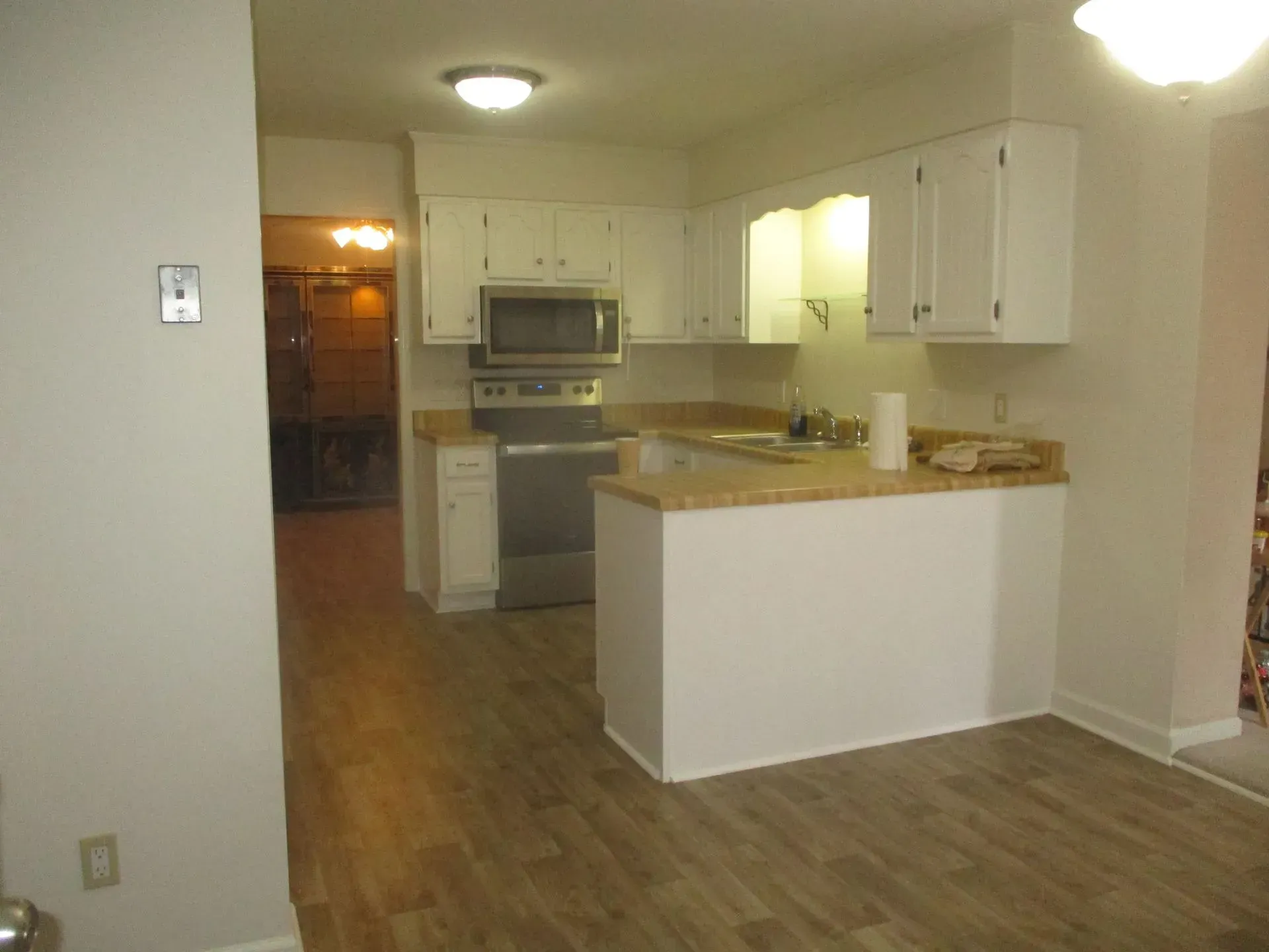 Empty apartment kitchen with white cabinets, tan countertops, and wood flooring