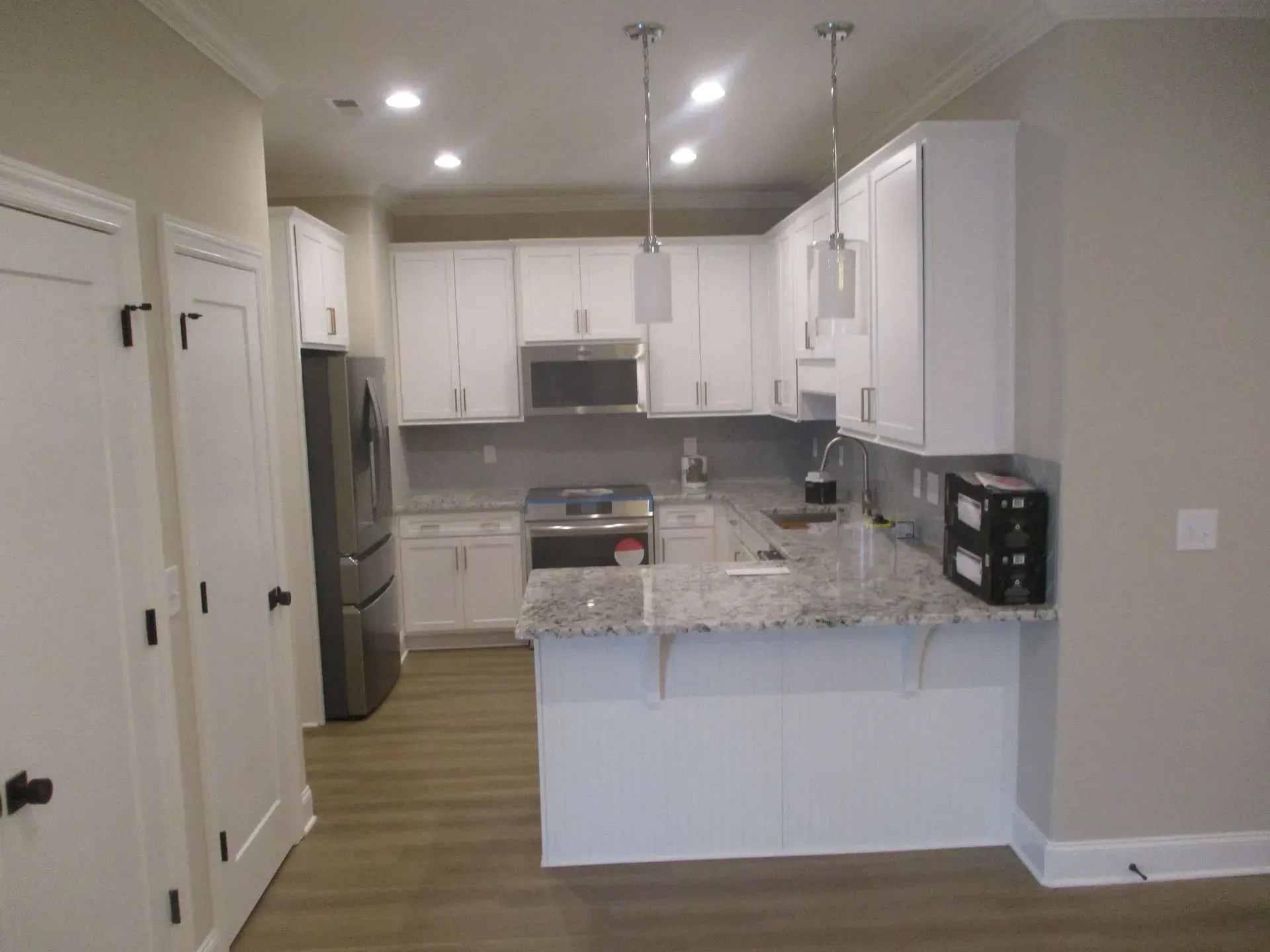Bright white kitchen with granite island, stainless fridge, and light wood flooring