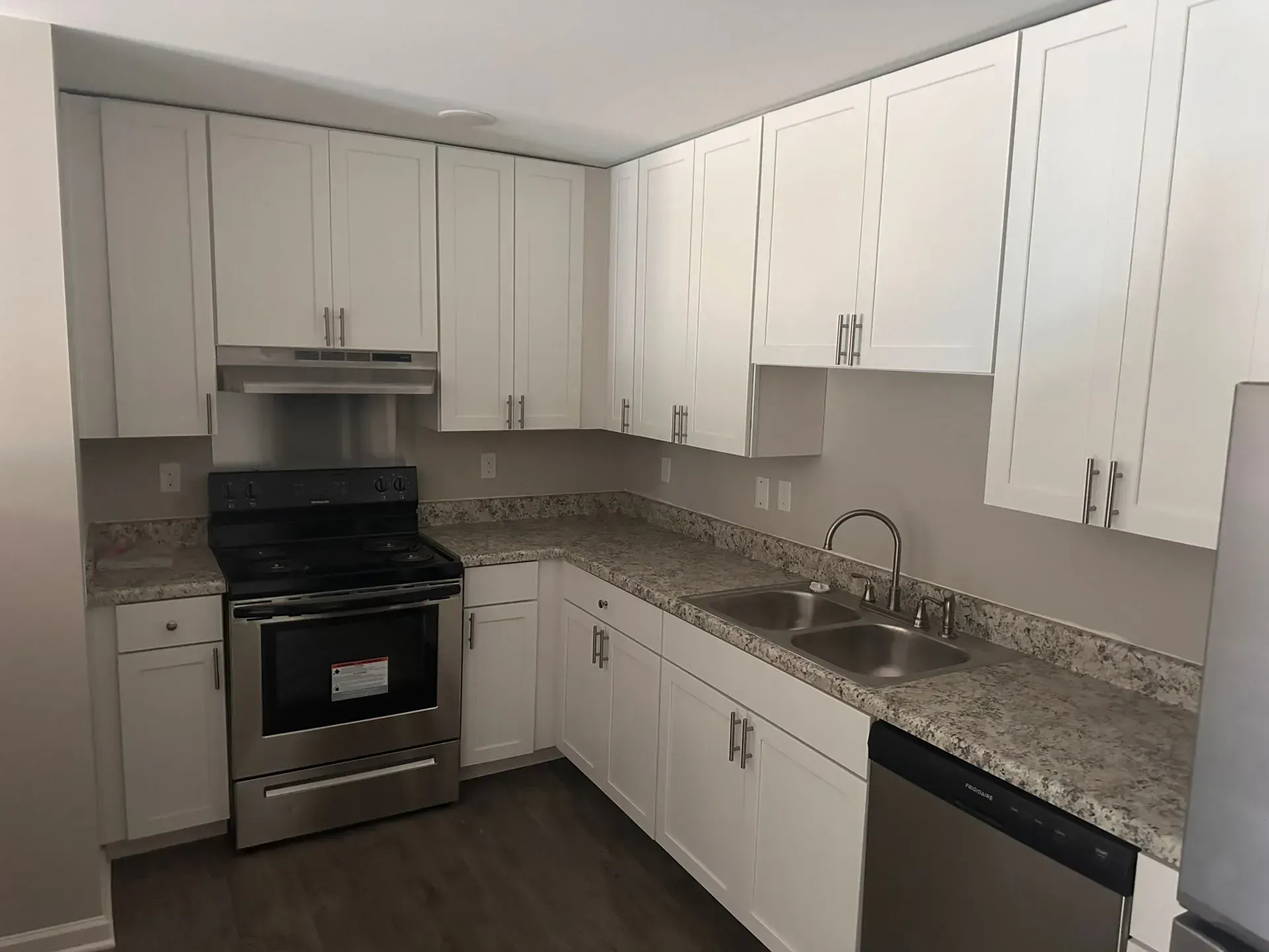 Modern kitchen with white cabinets, stainless steel stove, granite countertops, and sink under bright lighting