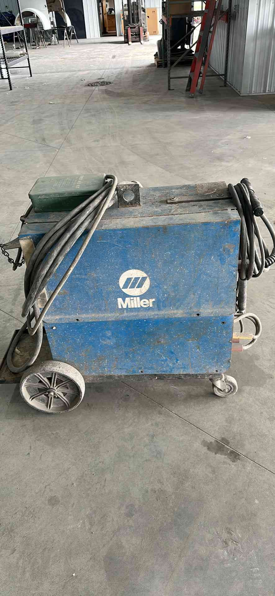 Blue Miller welding machine on wheels in a workshop.