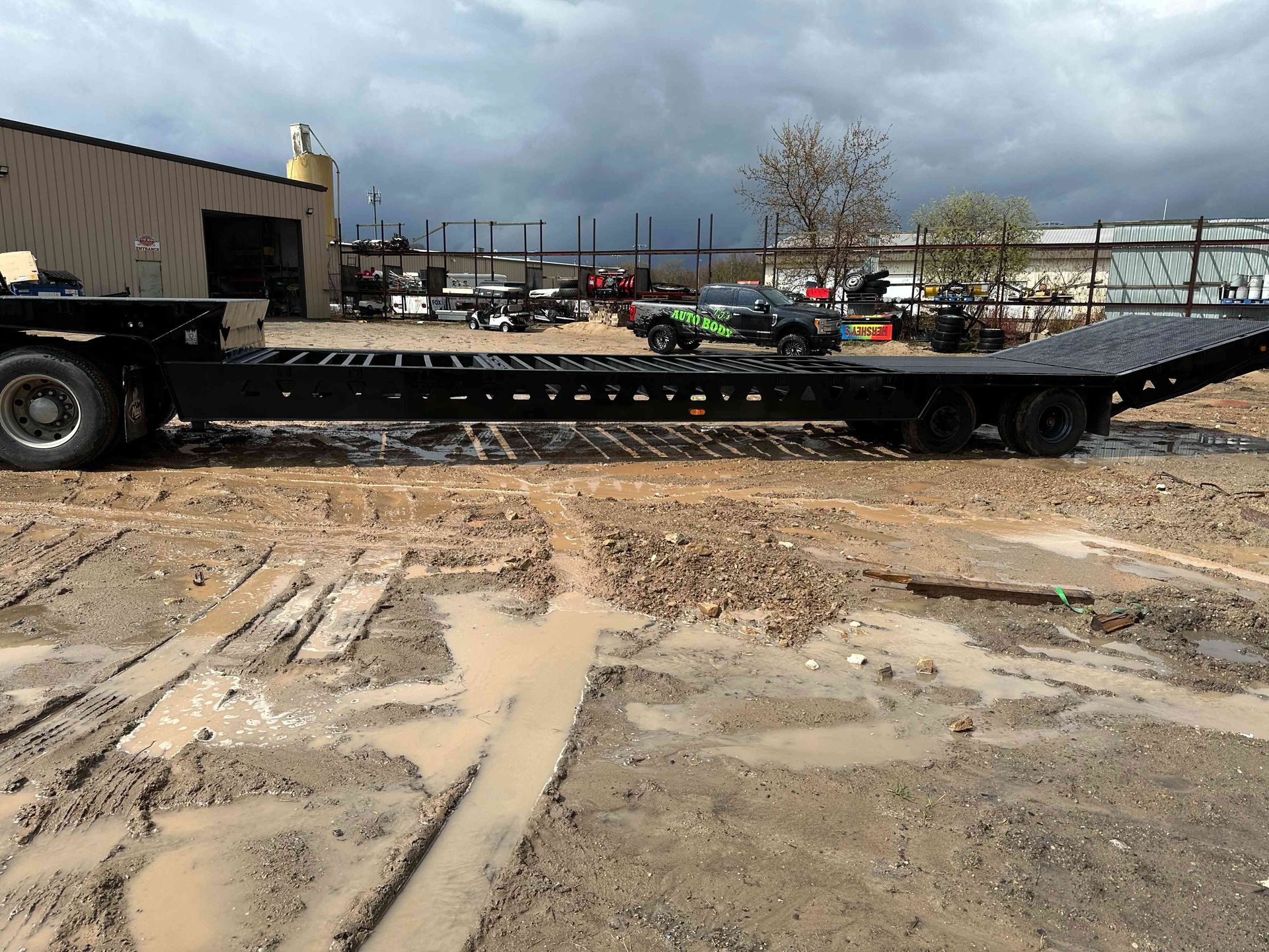 Flatbed tow truck on a muddy construction site under a cloudy sky