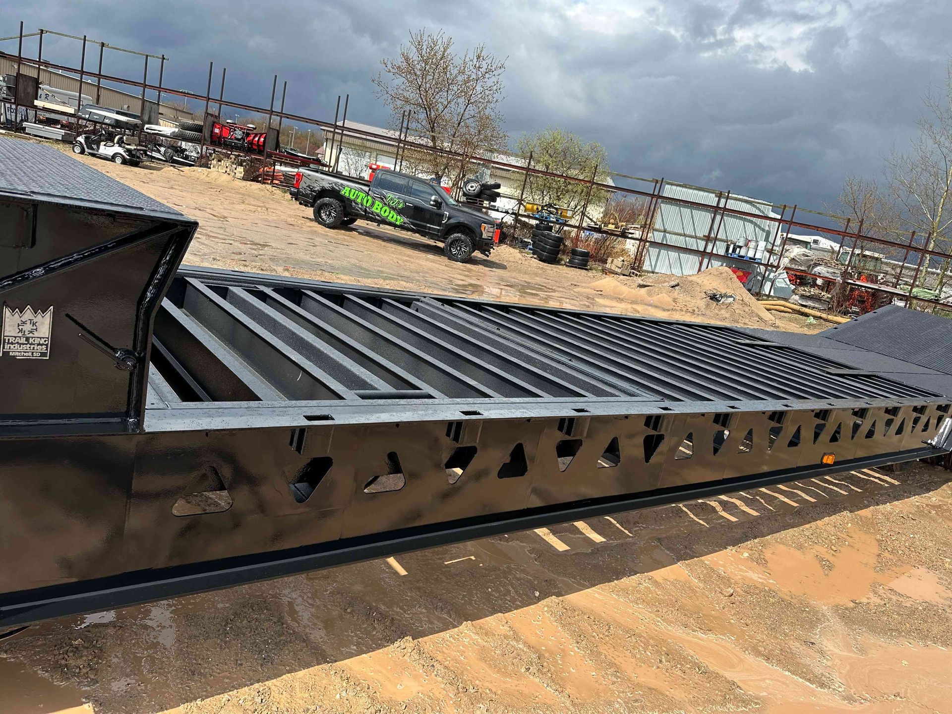 Metal framework under construction at an outdoor industrial site, with vehicles and cloudy sky in the background