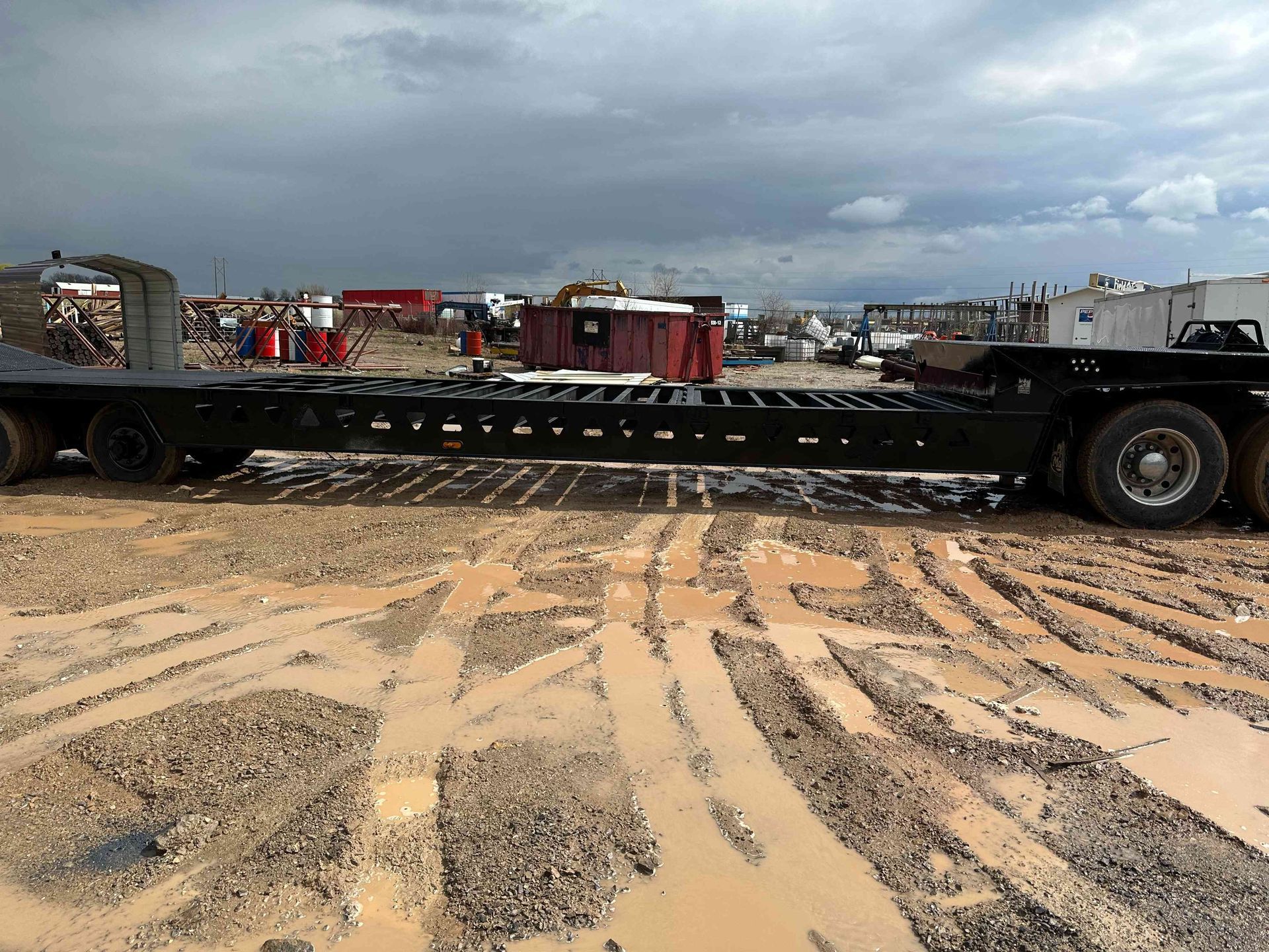 Large flatbed trailer on sandy ground at a construction site under cloudy skies