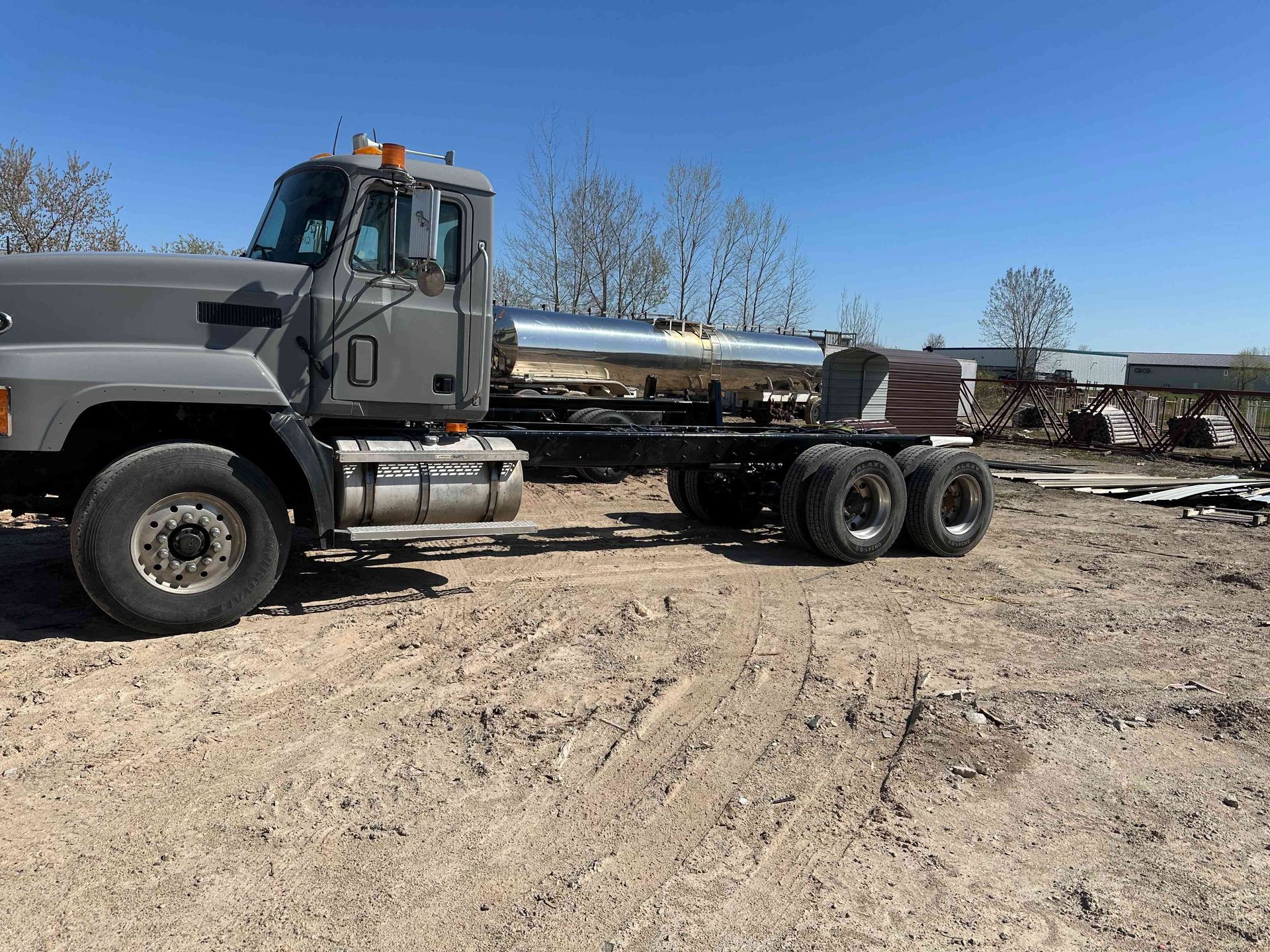 Black dump truck with flatbed trailer parked on a dirt lot under a clear blue sky.