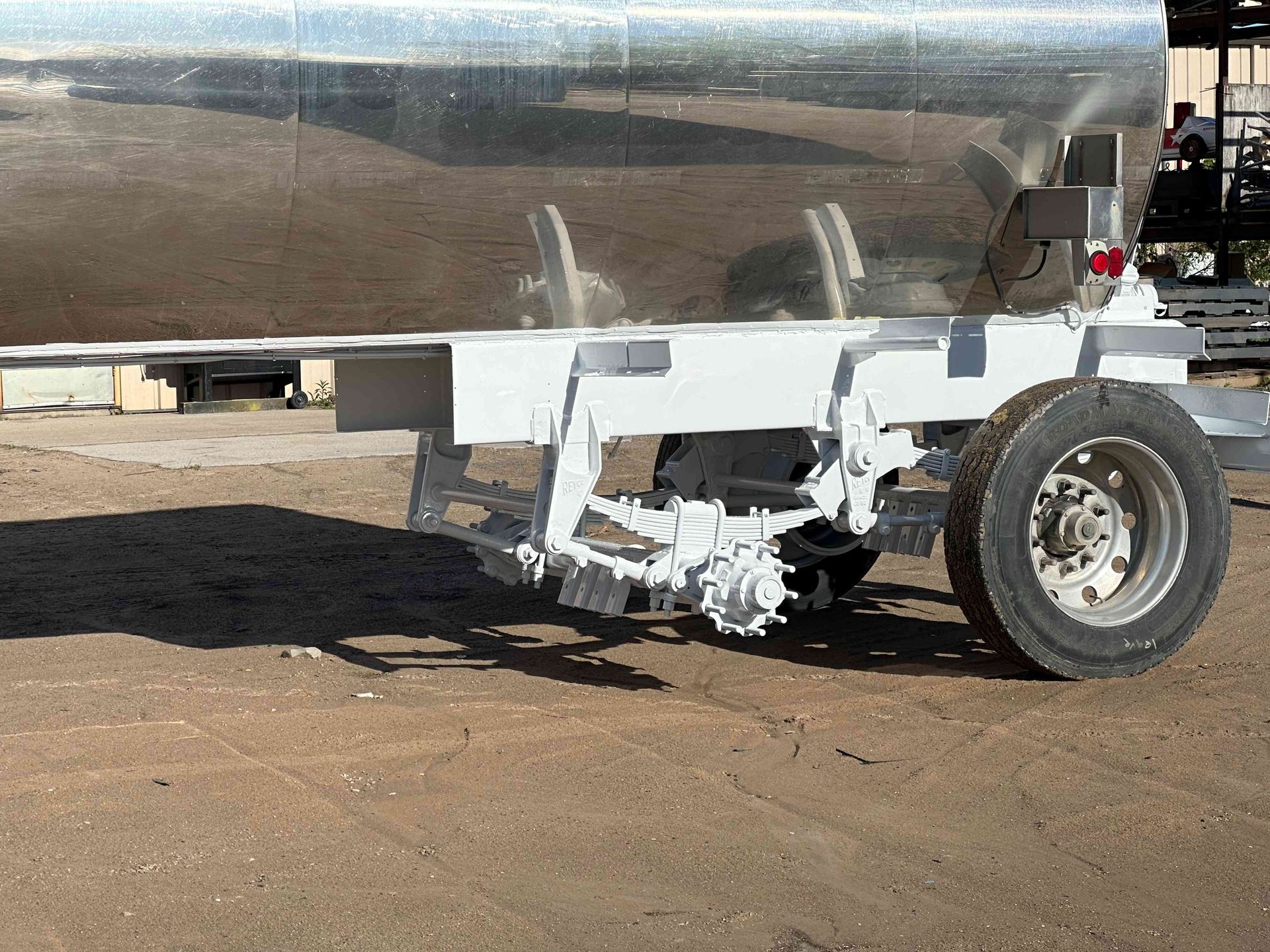 Silver tanker truck trailer on a dirt lot, showing the rear wheel and undercarriage.