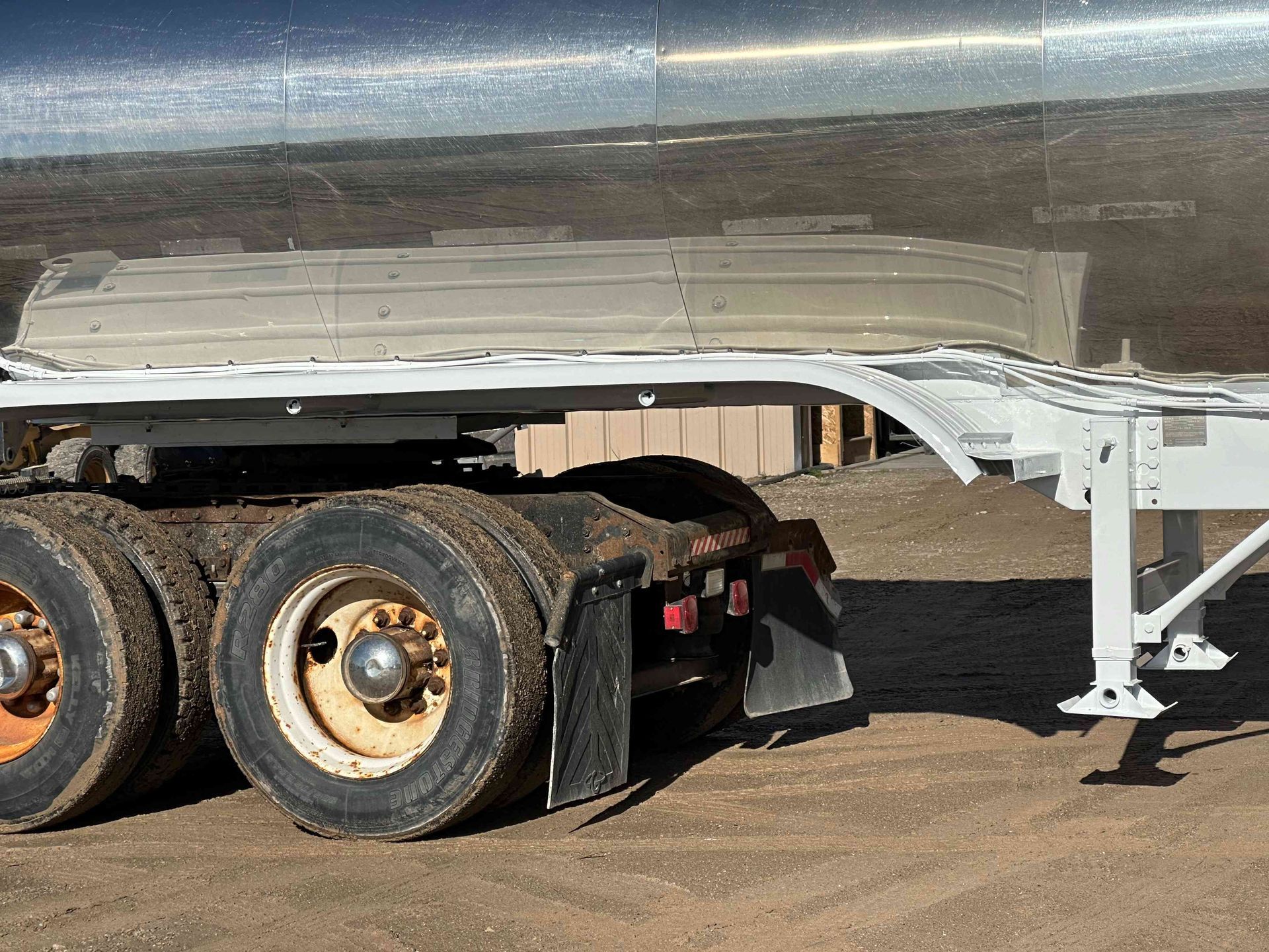 Semi-trailer parked on dirt, showing its wheels, landing gear, and metal tank body