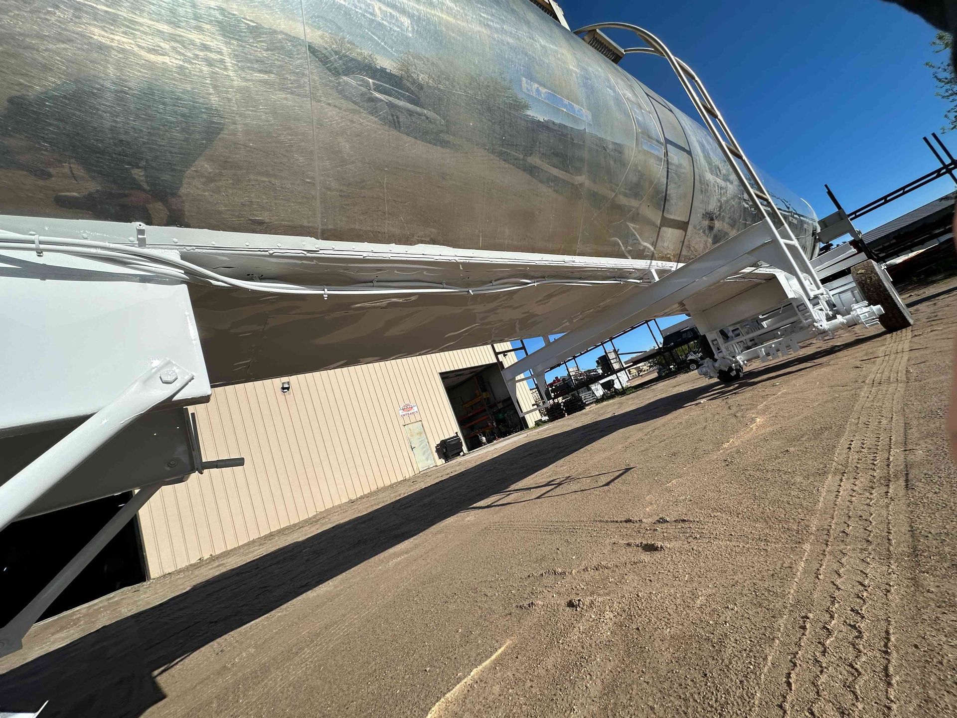 Large silver cylindrical tank or pipeline on supports beside a beige industrial building under a blue sky
