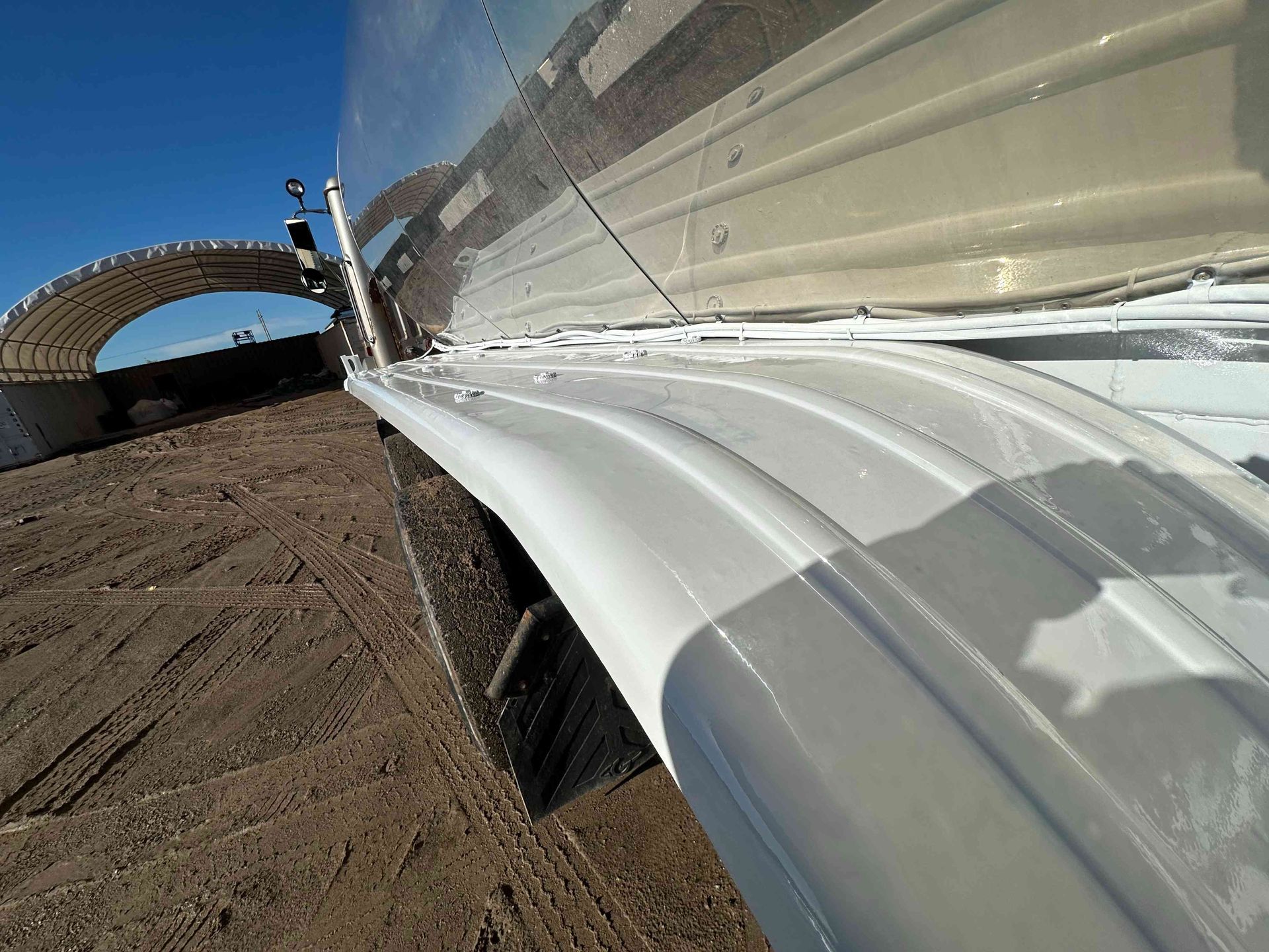 White metal guardrail running along a dirt road beside a bridge under a blue sky