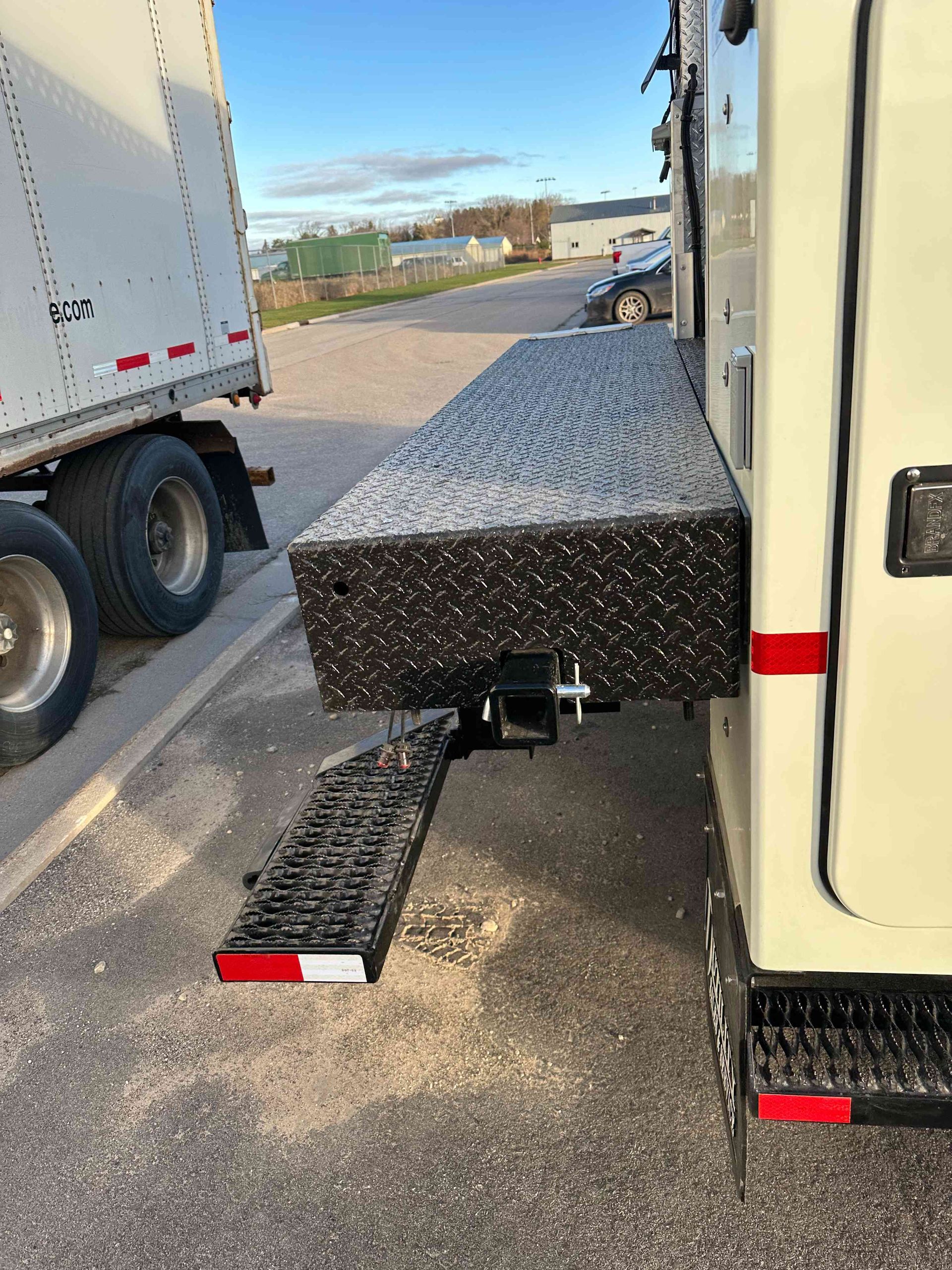 Truck with extended black metal ramp and platform parked beside a white trailer.