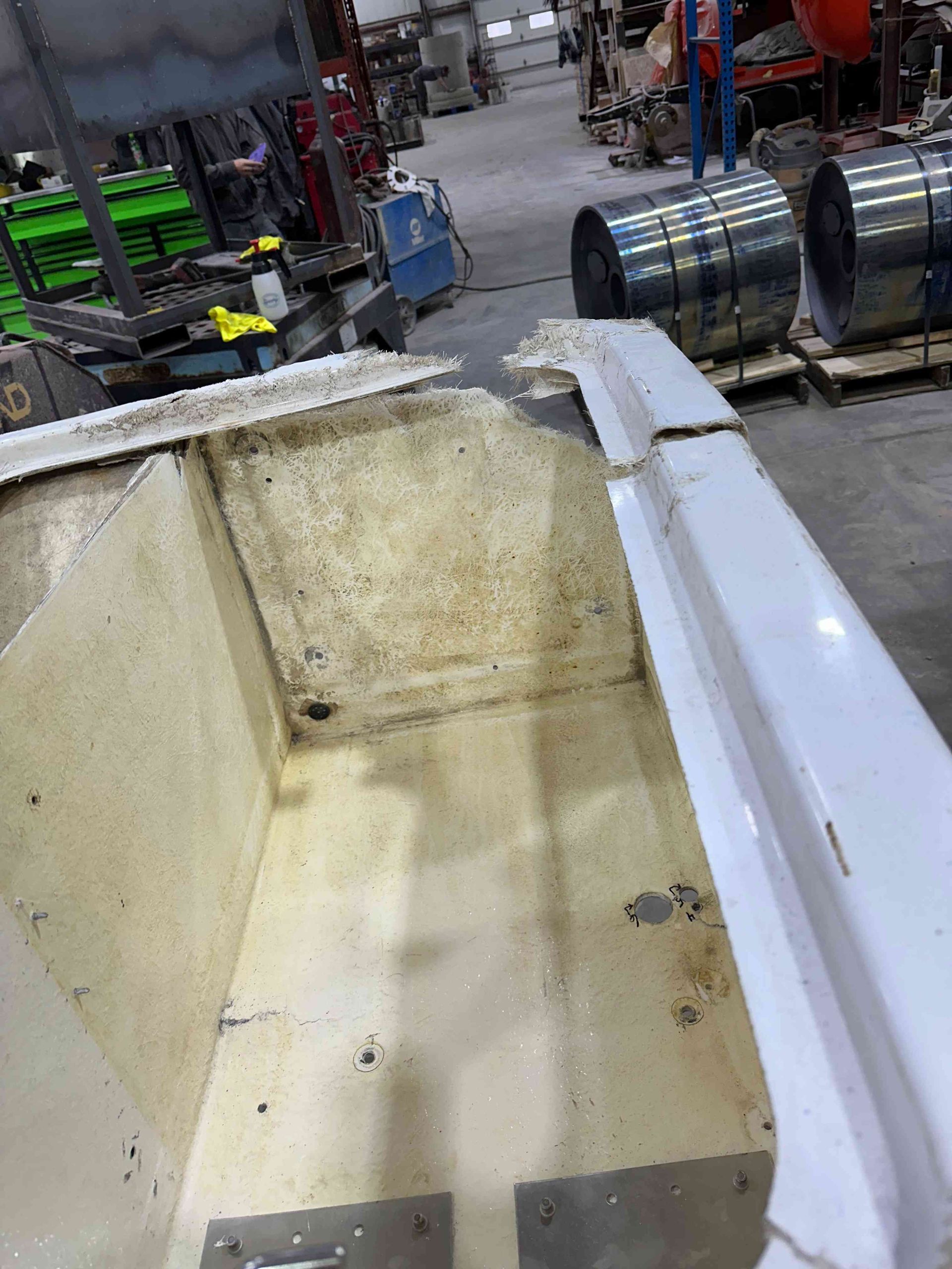 Dirty beige industrial bin or hopper in a workshop, with metal drums and equipment in the background
