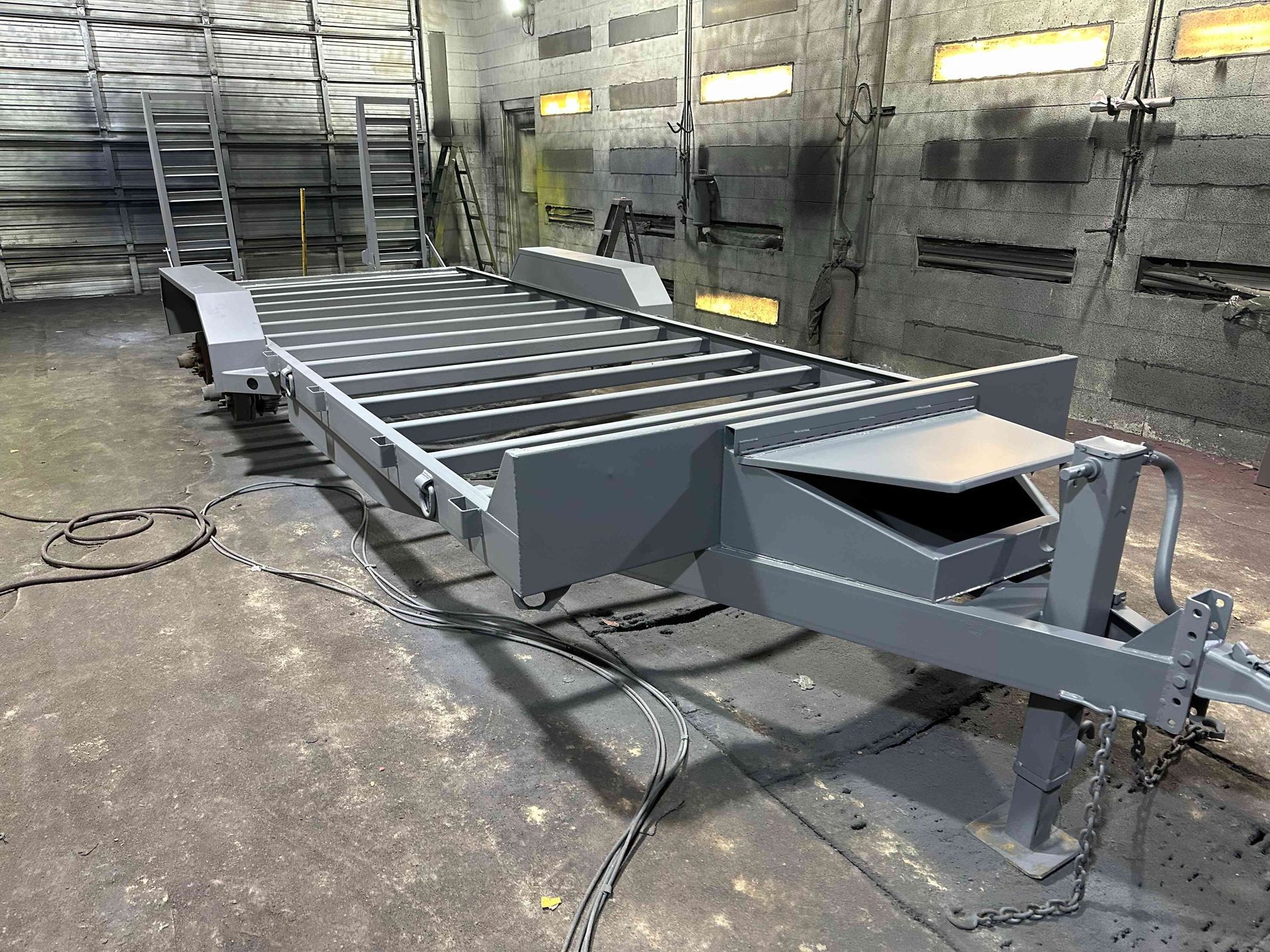 Metal conveyor line in a workshop, with gray rollers and a sloped platform on a concrete floor.