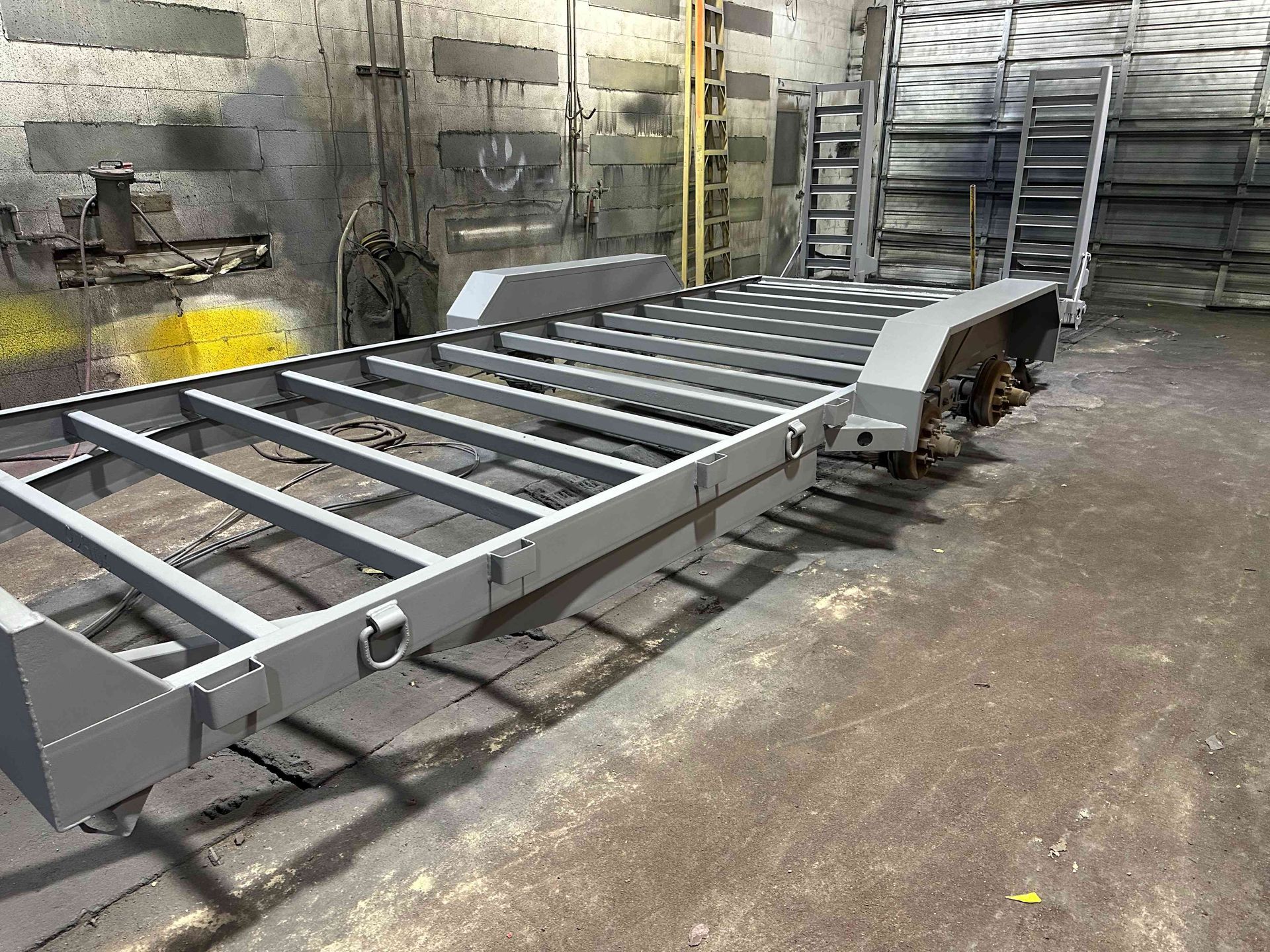 Large metal conveyor frame in a workshop, with silver rails and caster wheels on a concrete floor.