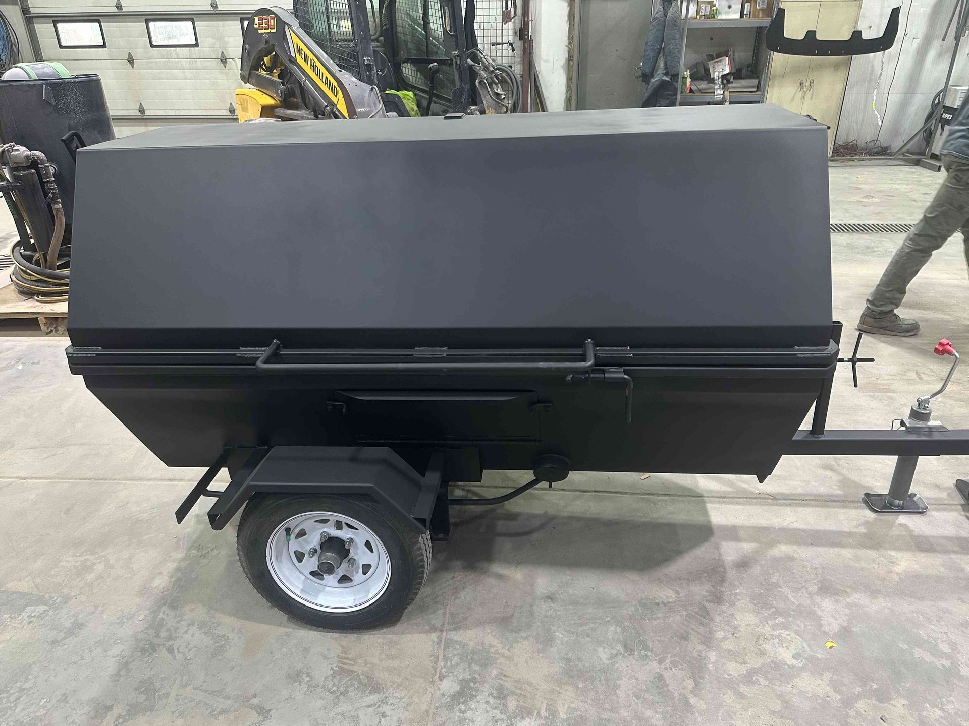 Black utility trailer with a closed cargo box in a workshop, hitched to a tow bar.