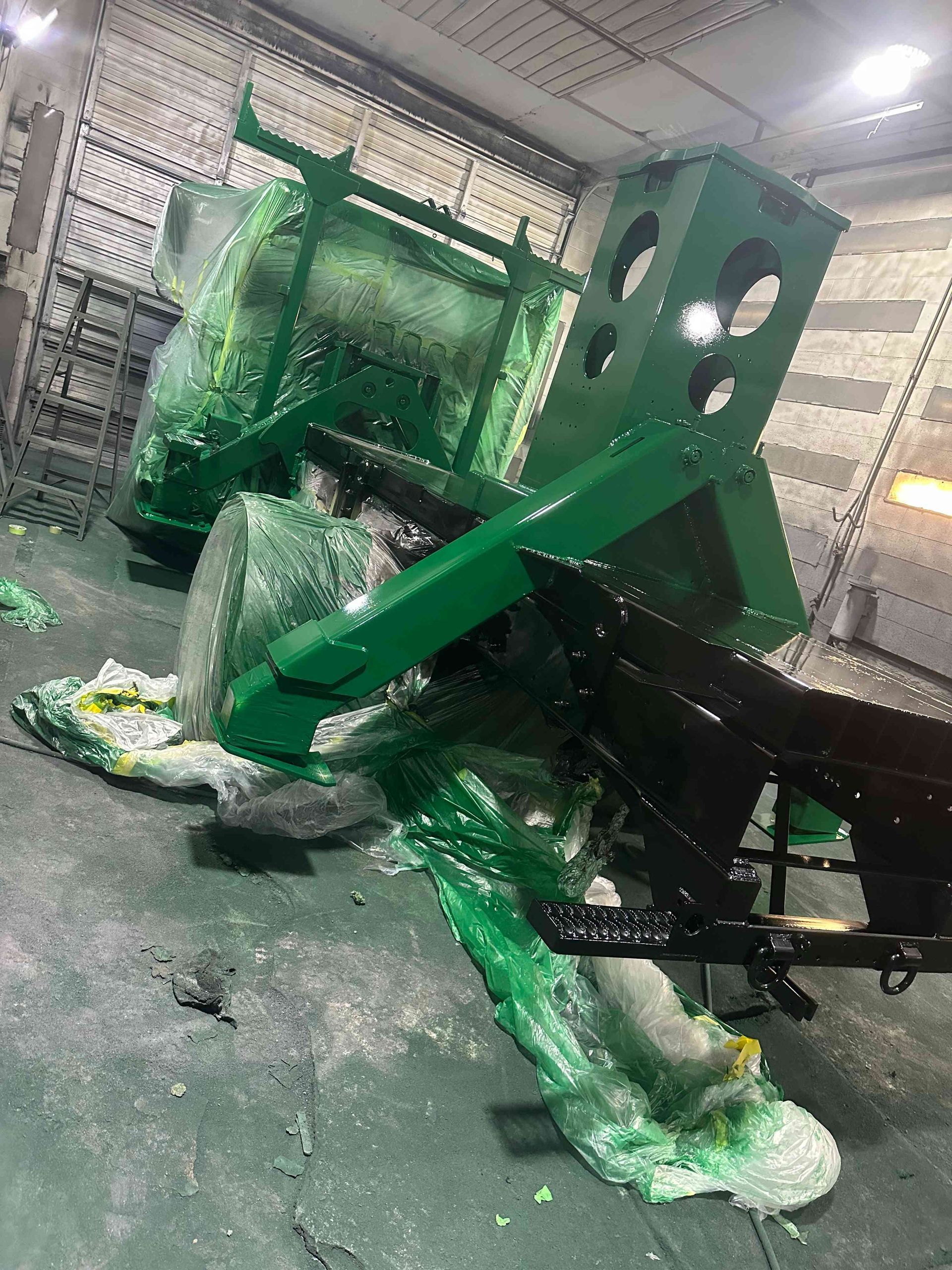 Green industrial machine covered in torn plastic and debris inside a warehouse or factory floor