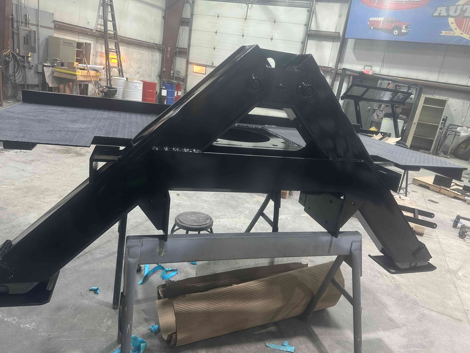 Black metal triangular frame in a workshop, with a bent metal panel leaning beneath it.