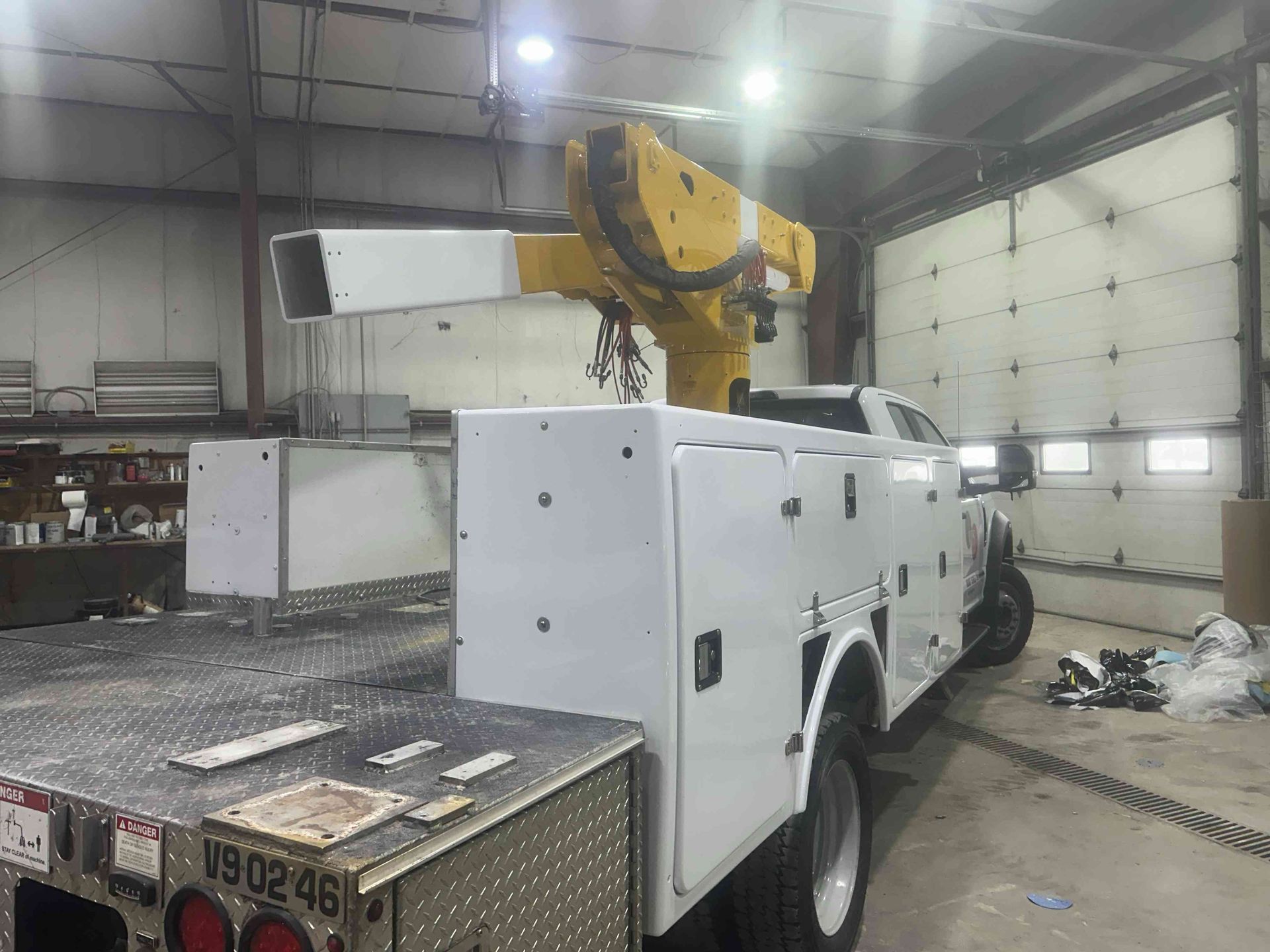 White utility truck with mounted crane in a warehouse garage, viewed from the rear side.