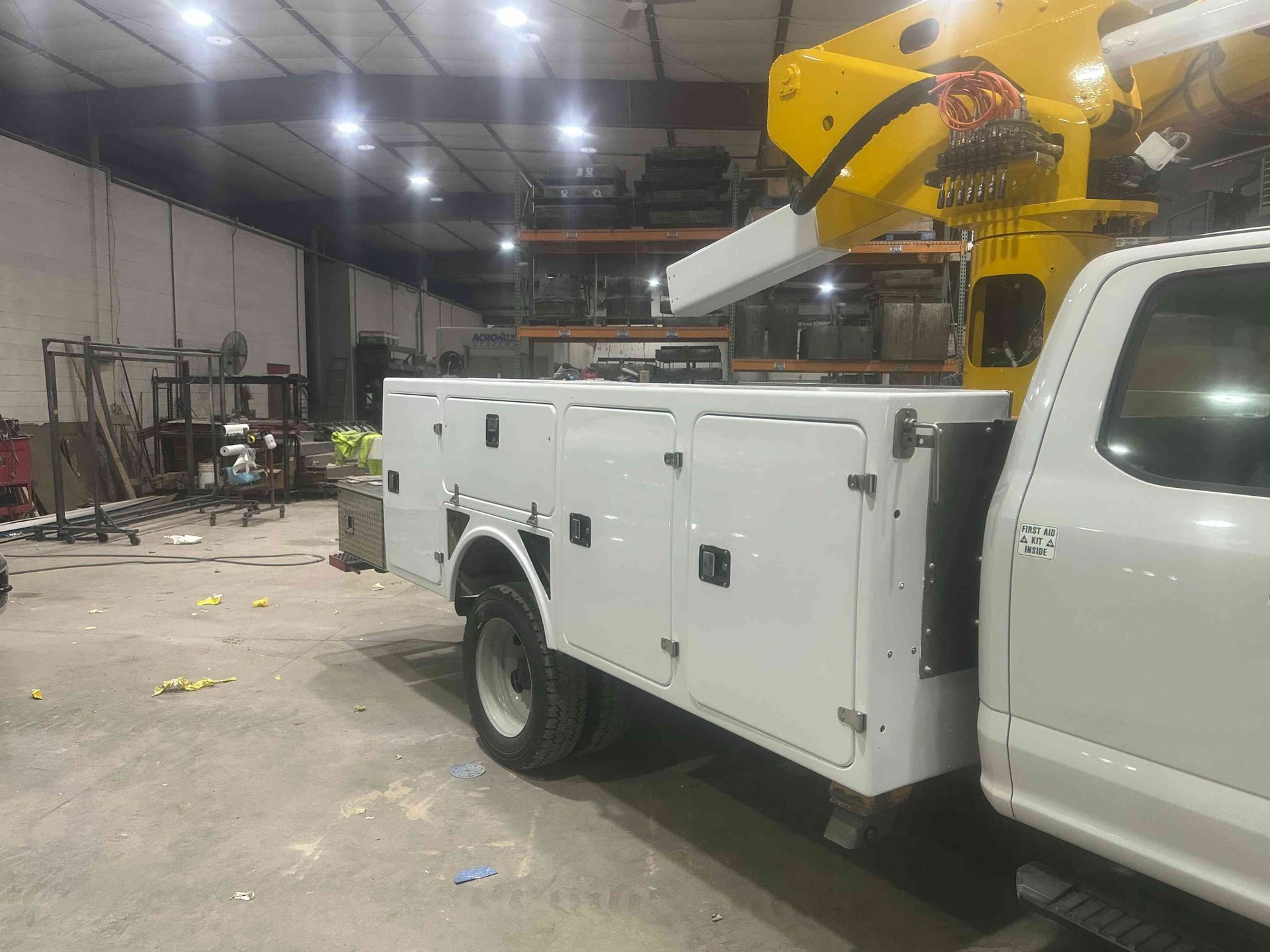 White utility truck with a yellow bucket lift parked inside an industrial warehouse.