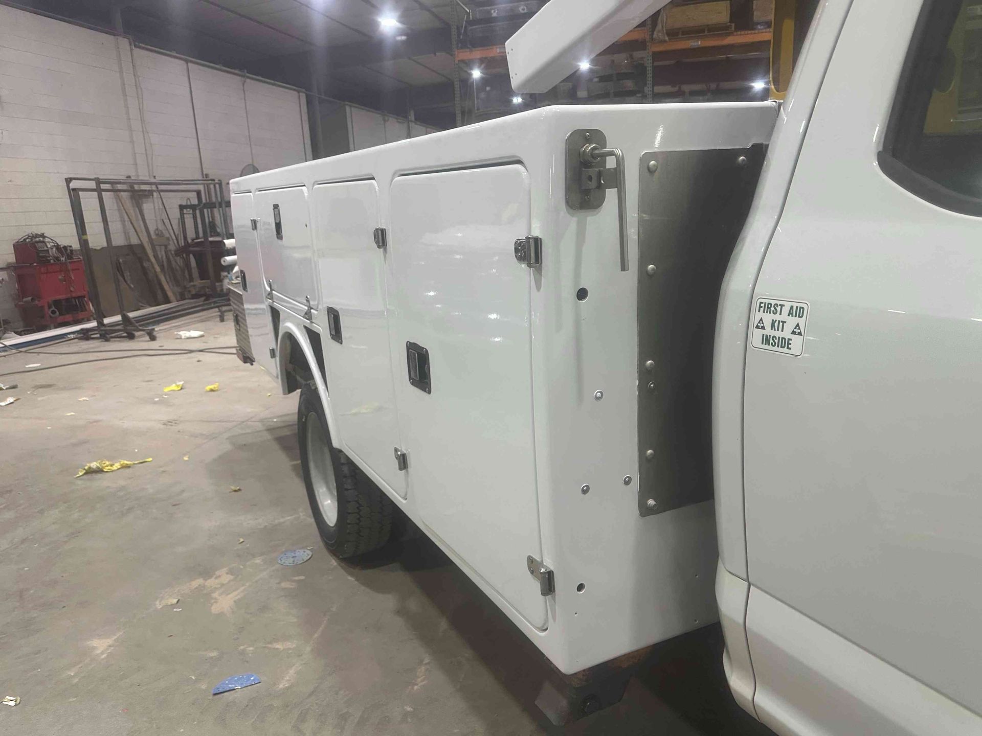 White utility truck with storage compartments parked inside an industrial warehouse.