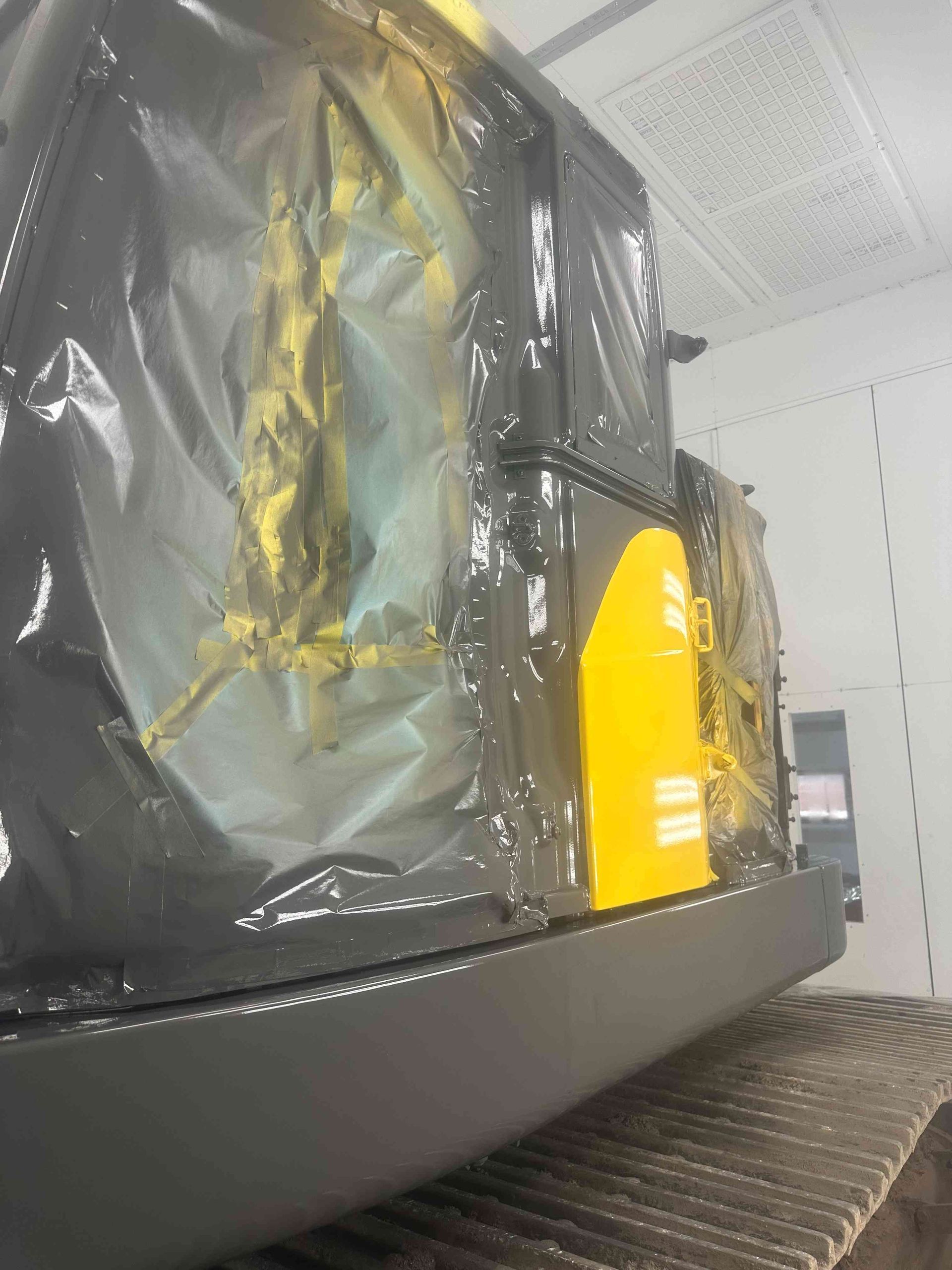 Black machine wrapped in plastic with a yellow panel, sitting in a workshop or paint booth