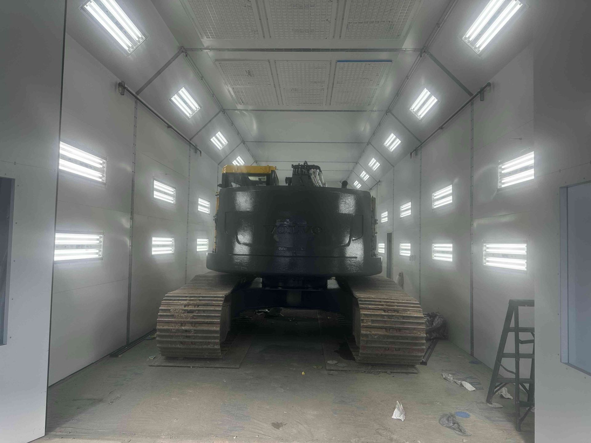 Military vehicle in a bright white spray booth or paint chamber, facing forward with tank treads visible.