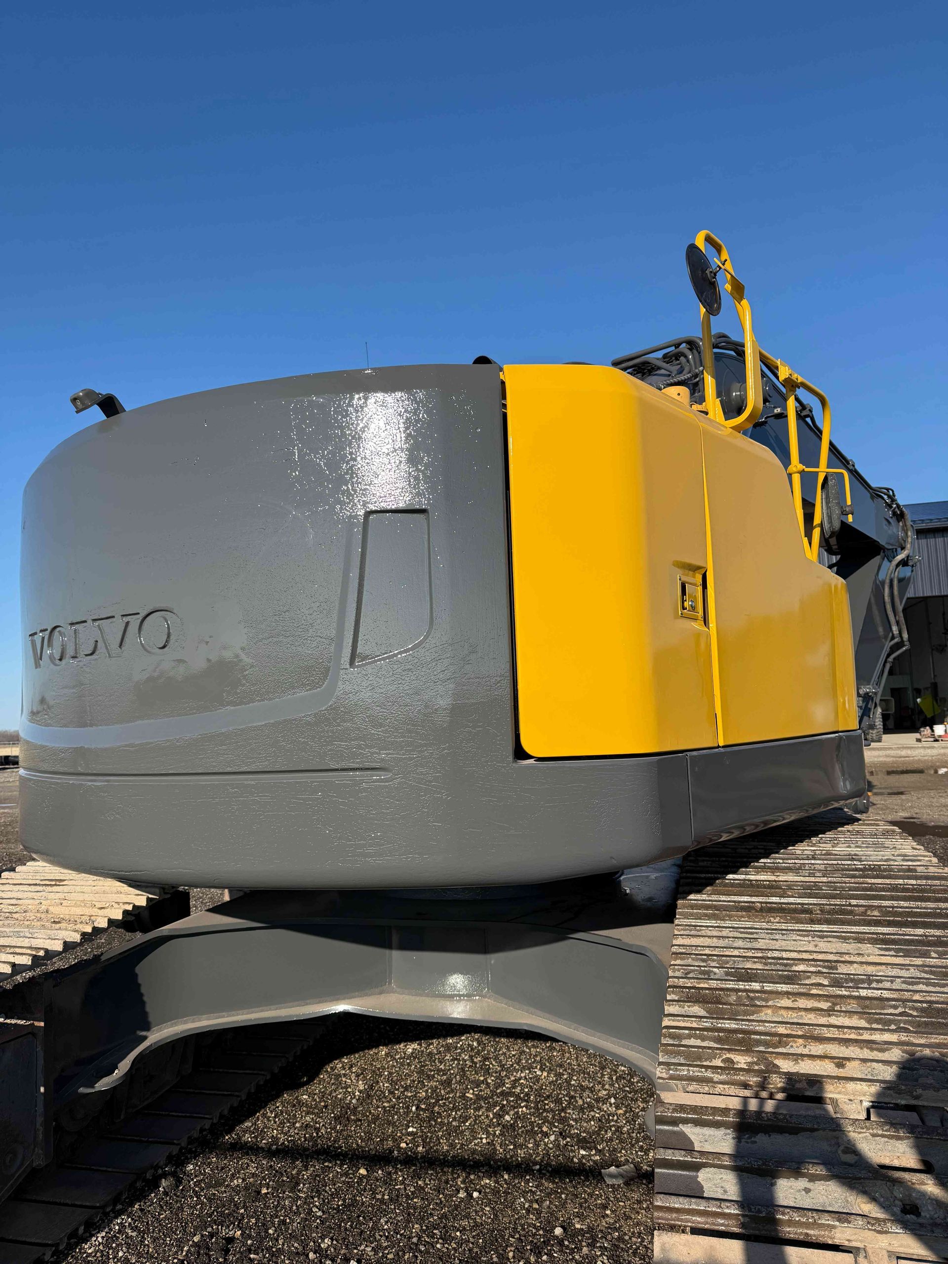 Yellow and gray excavator arm against a blue sky on a rocky worksite