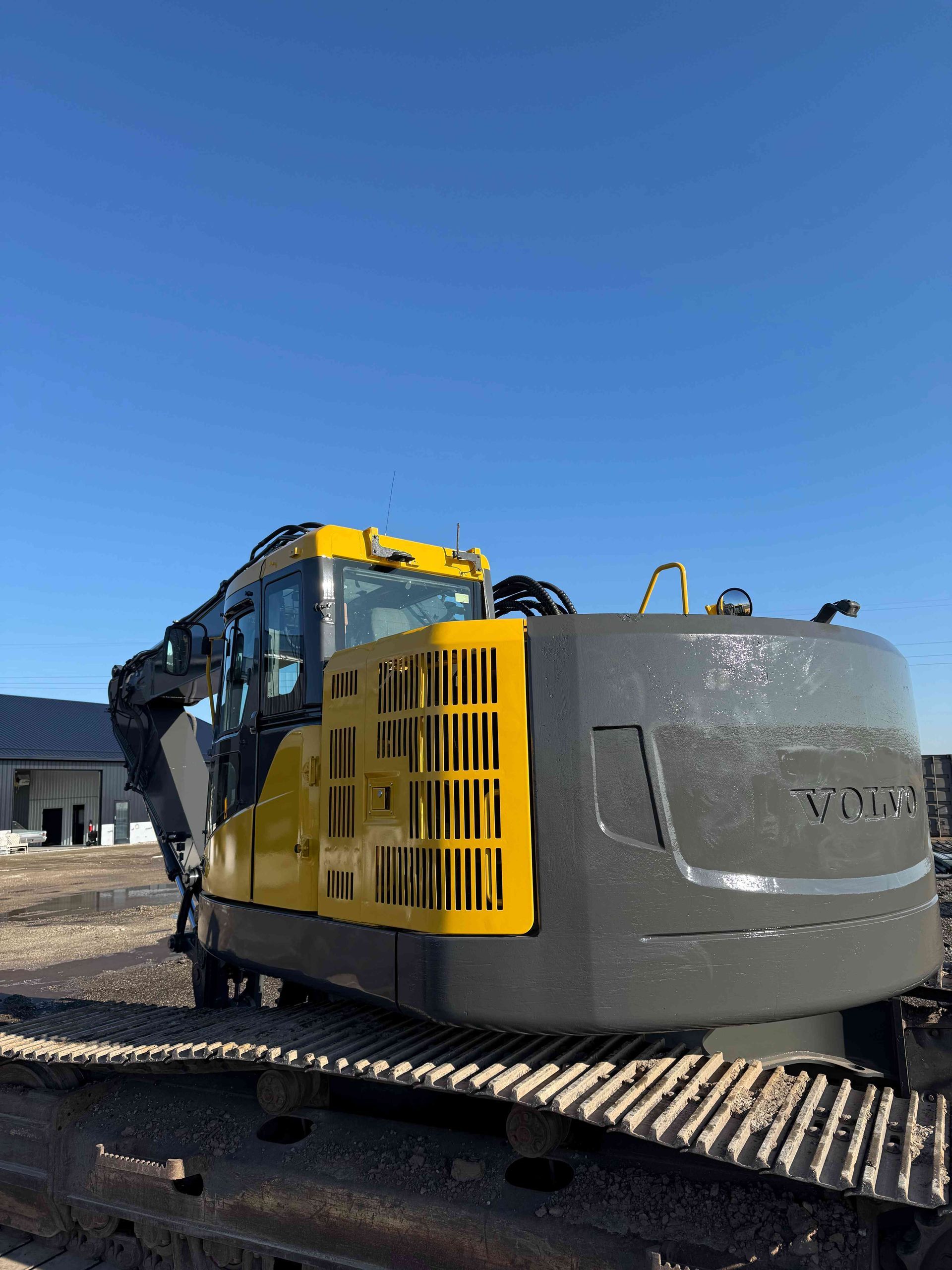 Yellow and gray excavator parked on gravel under a clear blue sky